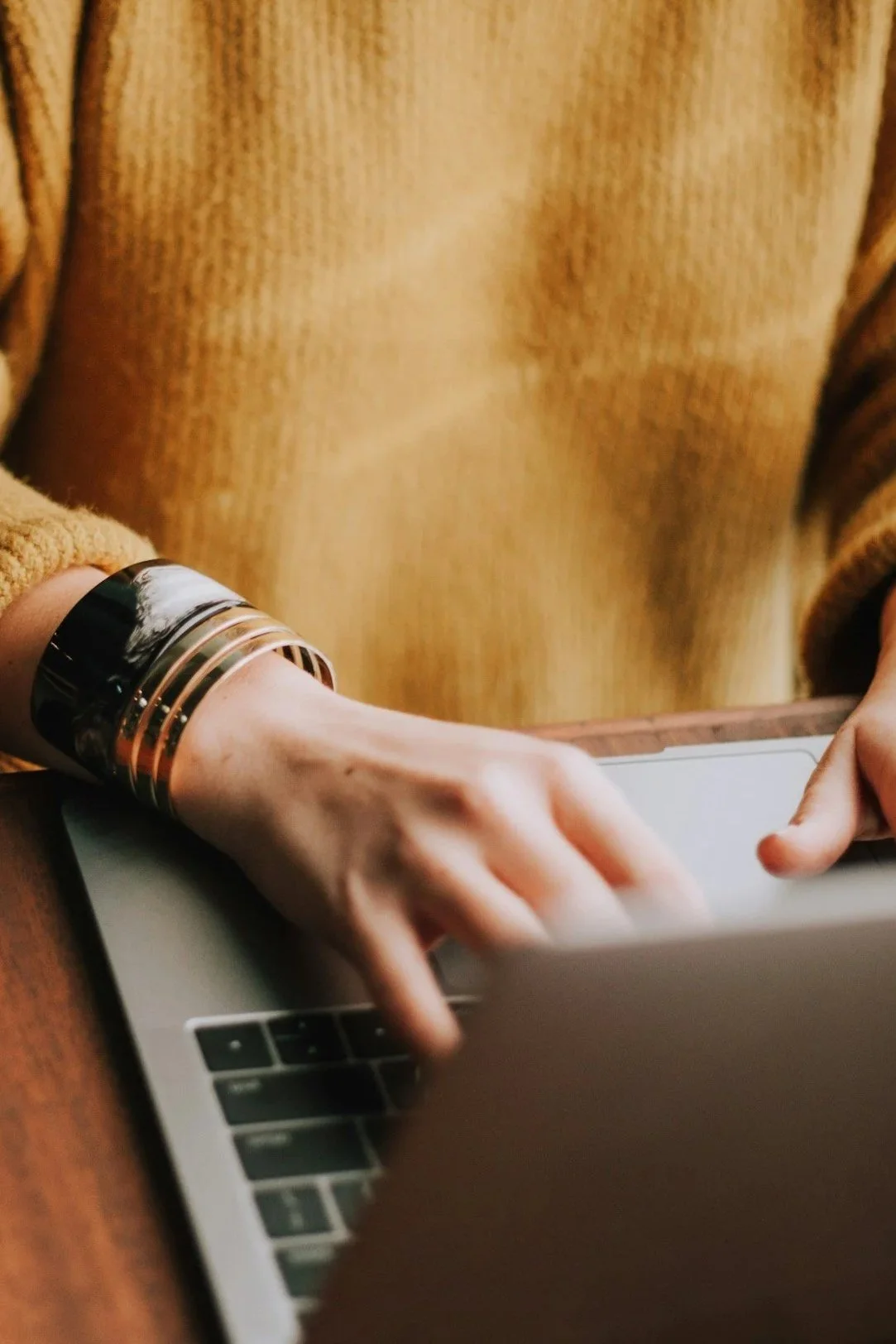 A person wearing a beige sweater and large bracelets on their wrist using a laptop computer.