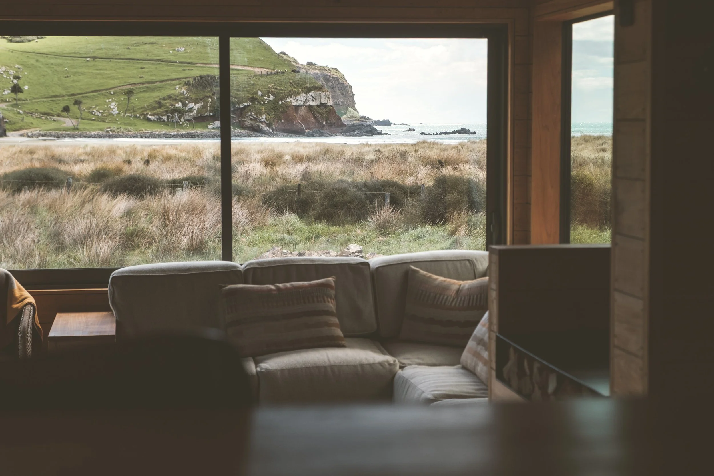 Living room with large window overlooking grassy dunes, cliffs, and ocean shoreline.