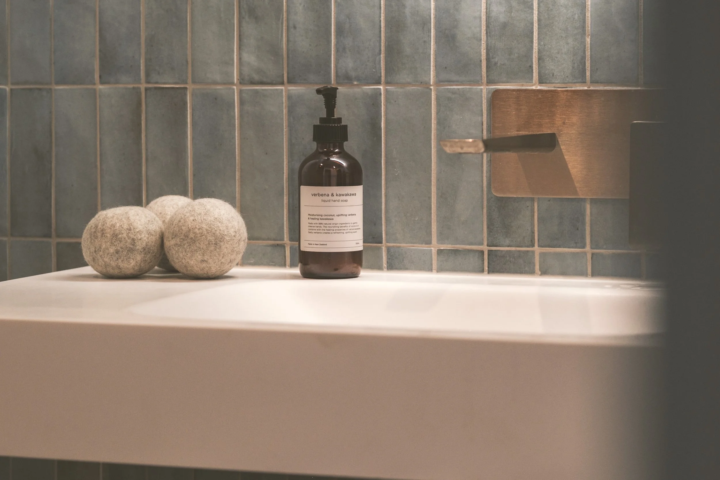 A bathroom sink with two felted balls and a bottle of liquid soap against a tiled wall.
