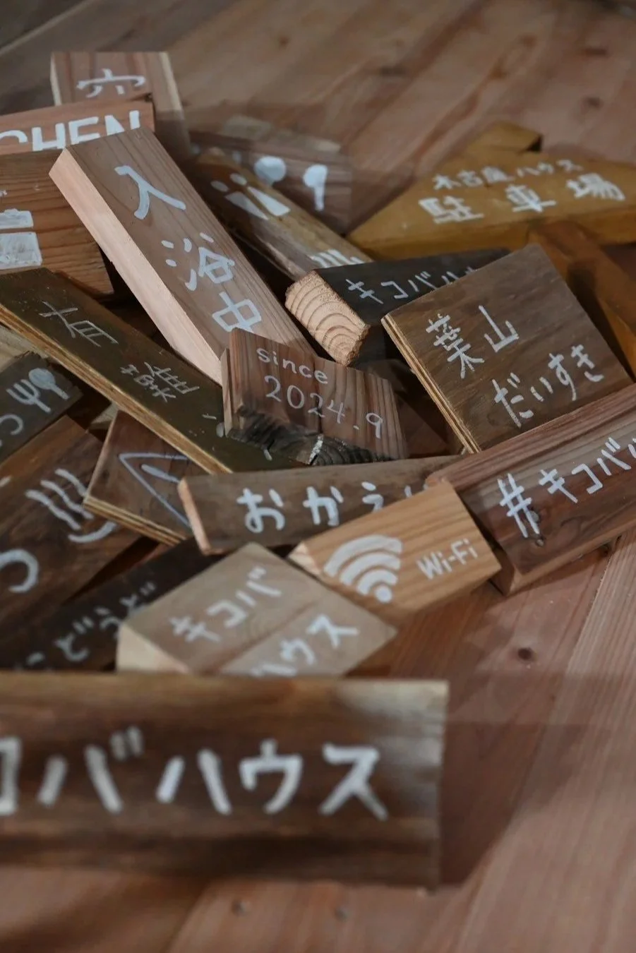 木製の小さな看板がいくつも置かれている。いくつかには日本語の文字とともにWi-Fiやsince 2024.9と記されているものもある。