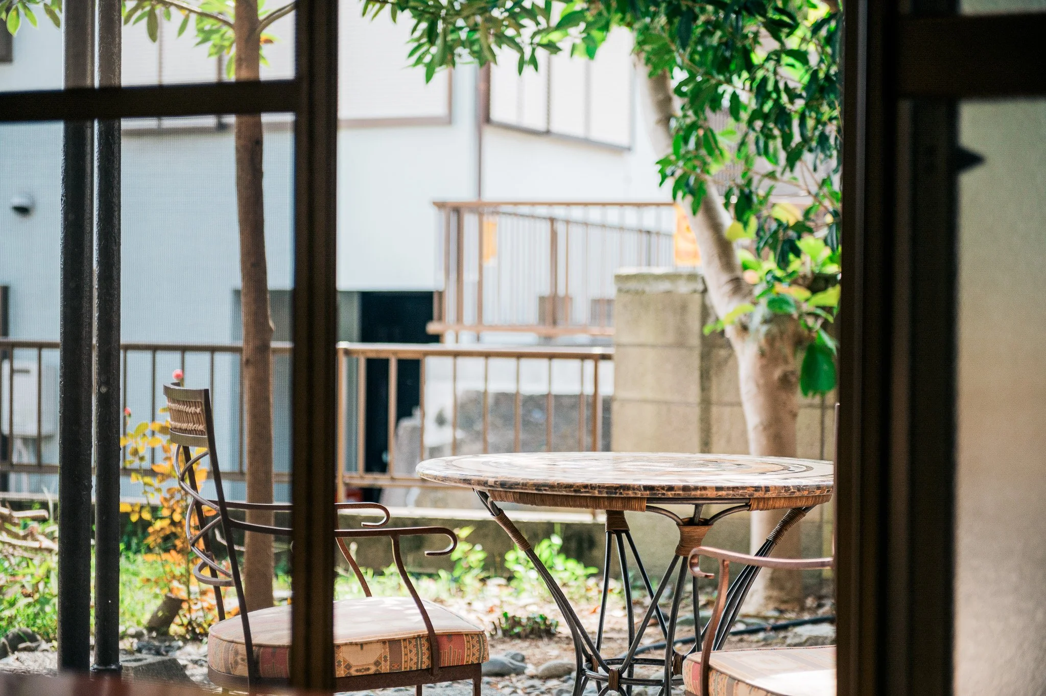 室内から見た庭のテーブルと椅子、外に木や植物が見える