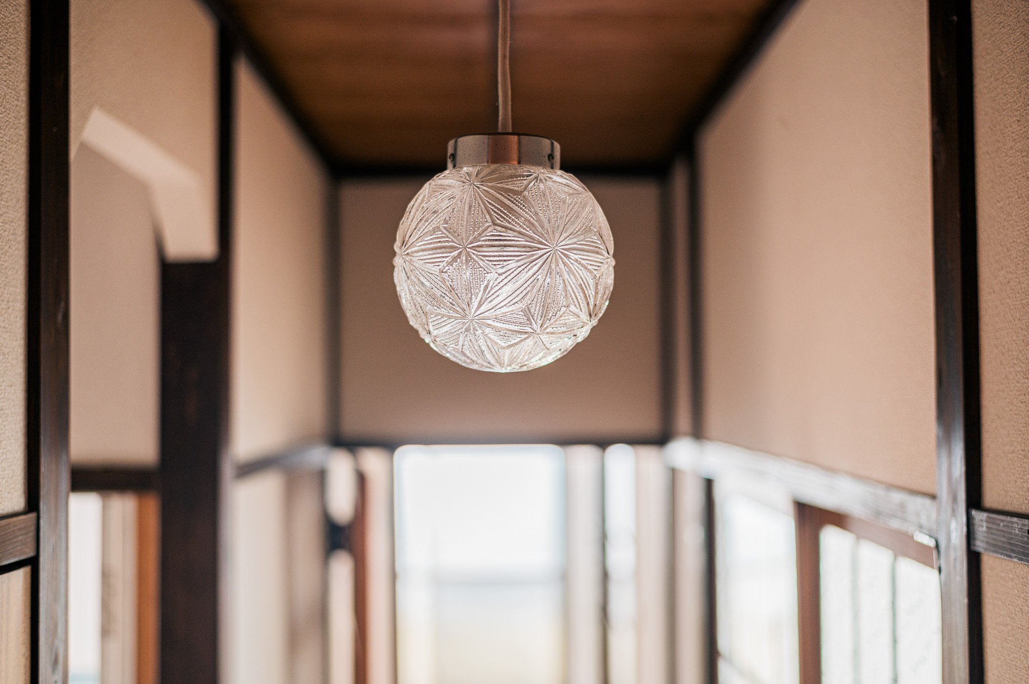 木造の廊下の天井に設置されたガラス製の照明器具。