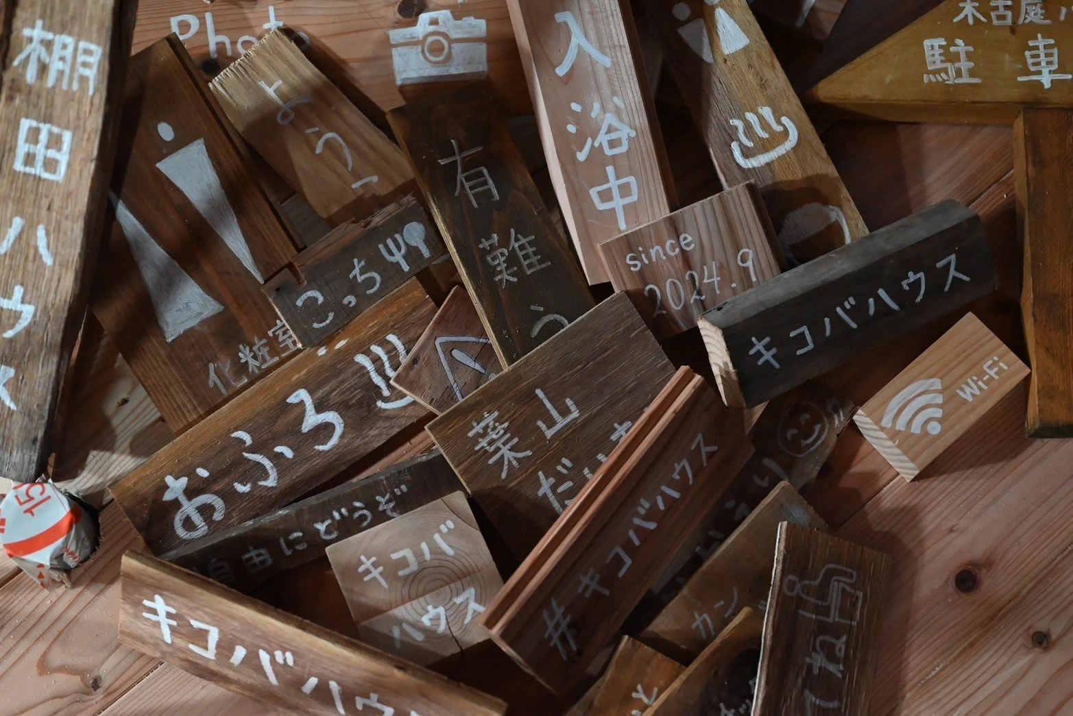 木製のサインと看板が積み重ねられた写真。いくつかのサインには日本語と英語の文字が書かれている。