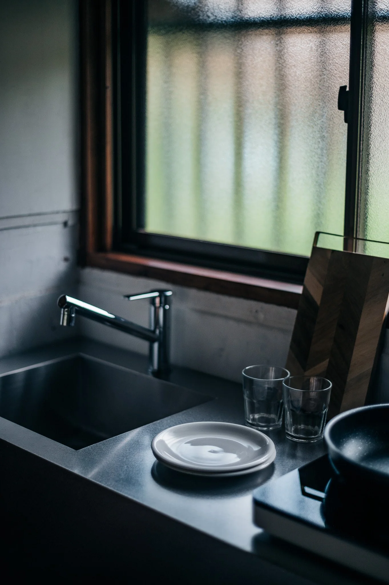 キッチンのシンクとカウンター。窓から自然光が差し込み、食器やグラスが置かれている静かな室内の風景。