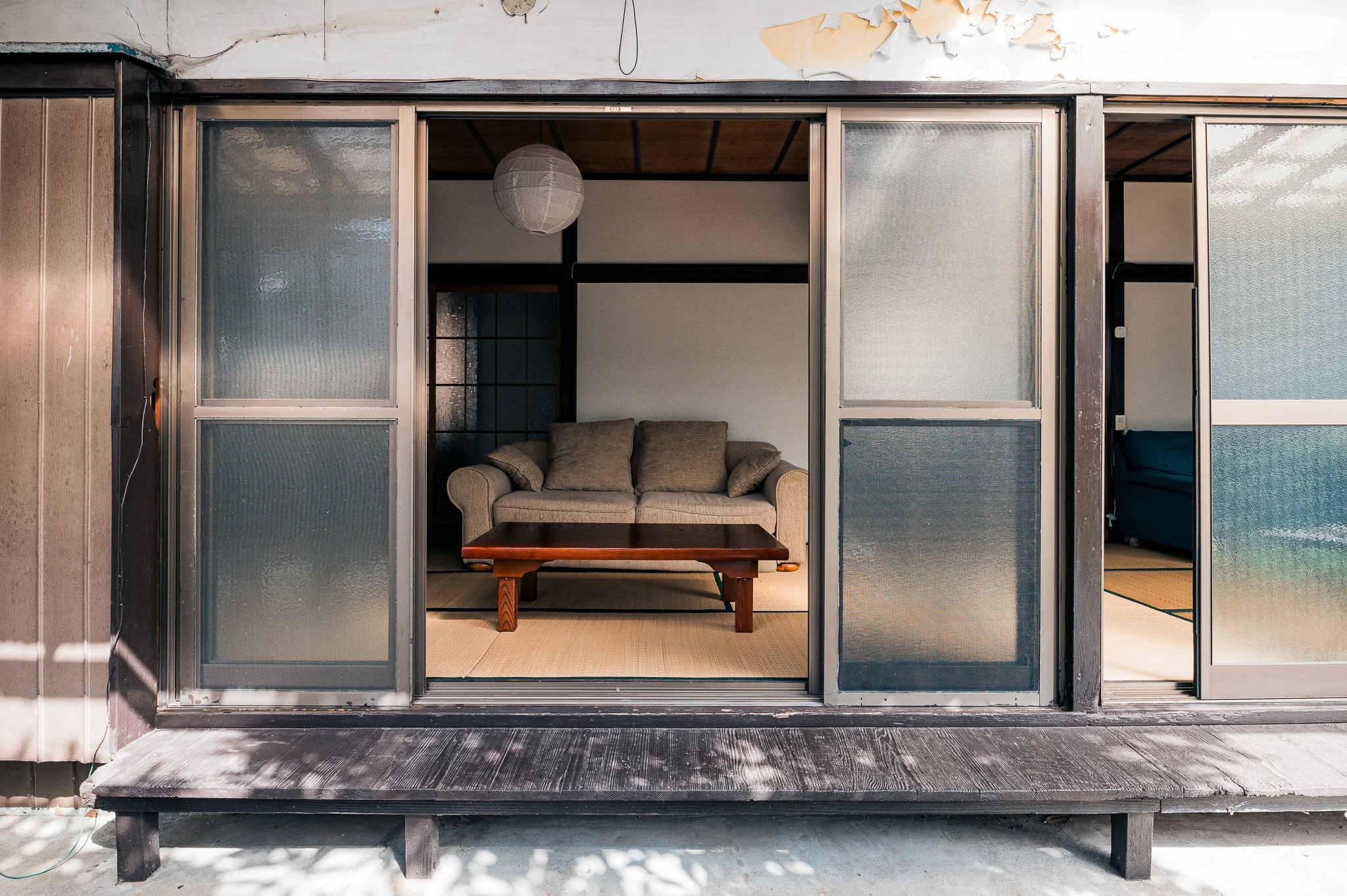 古い木製の縁側のある和風の家の内観、中央にソファと低い木のテーブルが配置されている。天井には白い紙のランプが吊るされている。