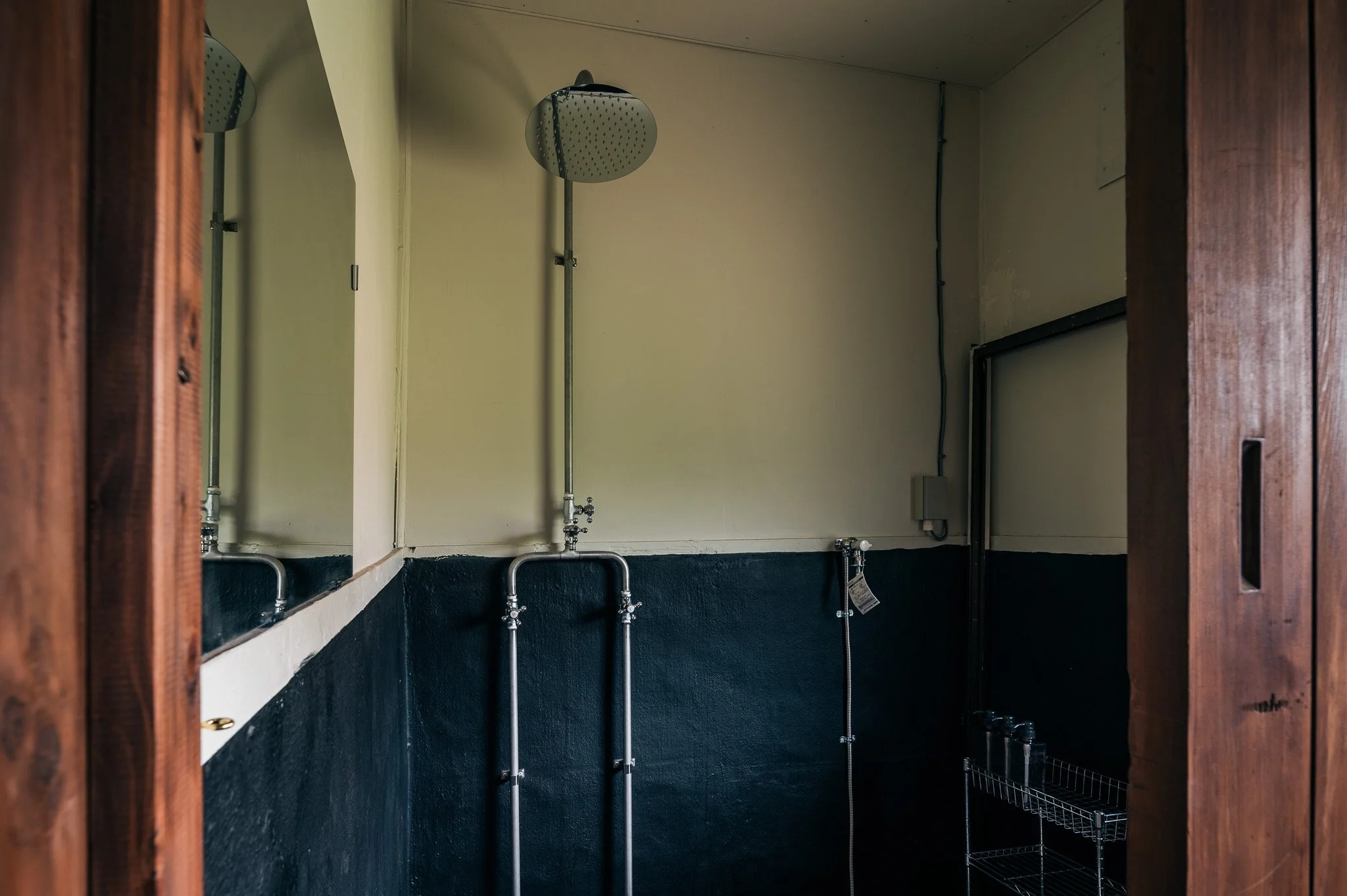 シャワールームの天井からの視点。二つのシャワーヘッドと壁に取り付けられた金具やラックが見える。