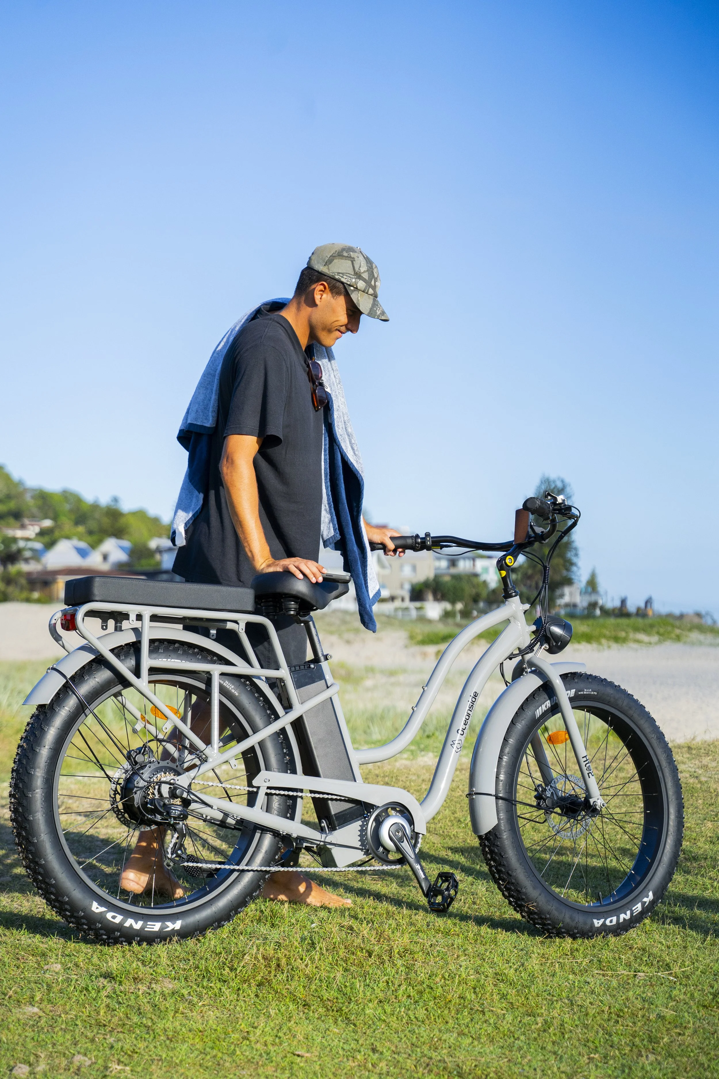A man standing outdoors with a white electric bike on a grassy area.