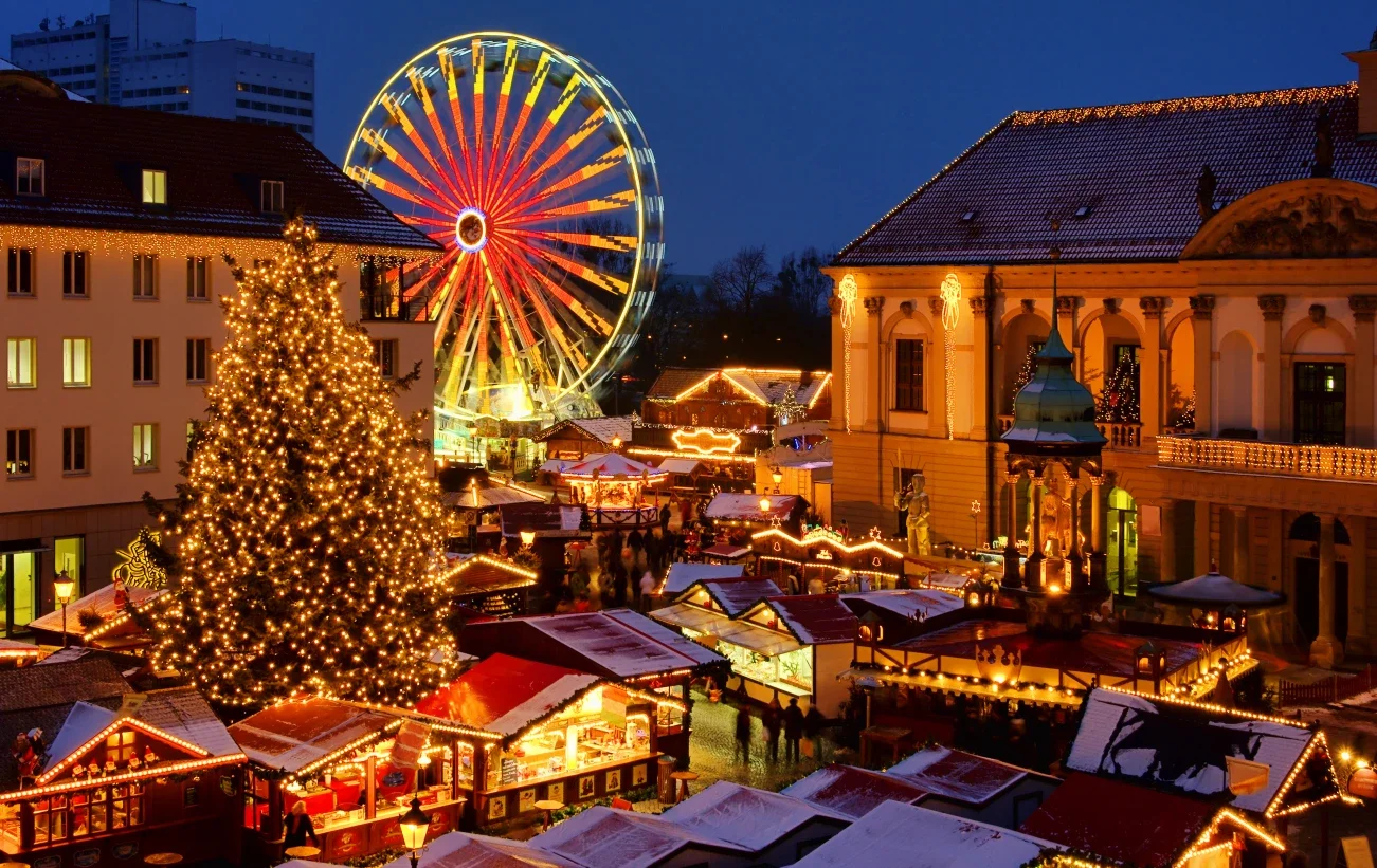 European Christmas market at night with festive lights Ferris wheel and holiday village featured by Ruggles & Routes Travel Co