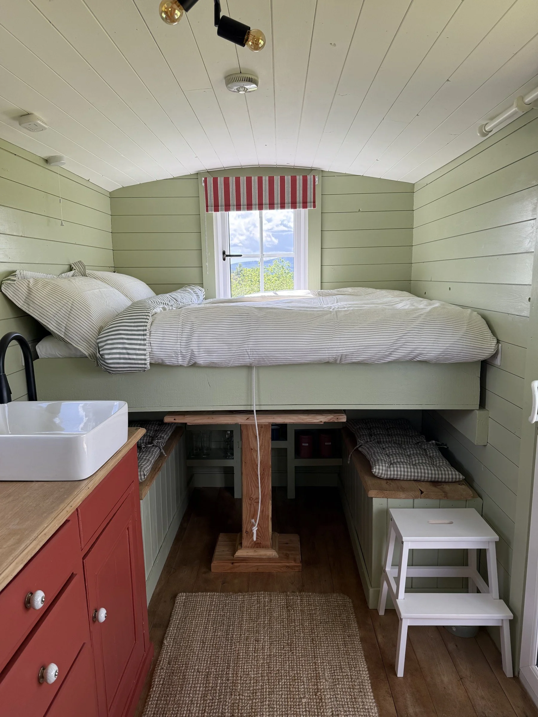 A cosy raised small double bed, with a stepping stool for access.
