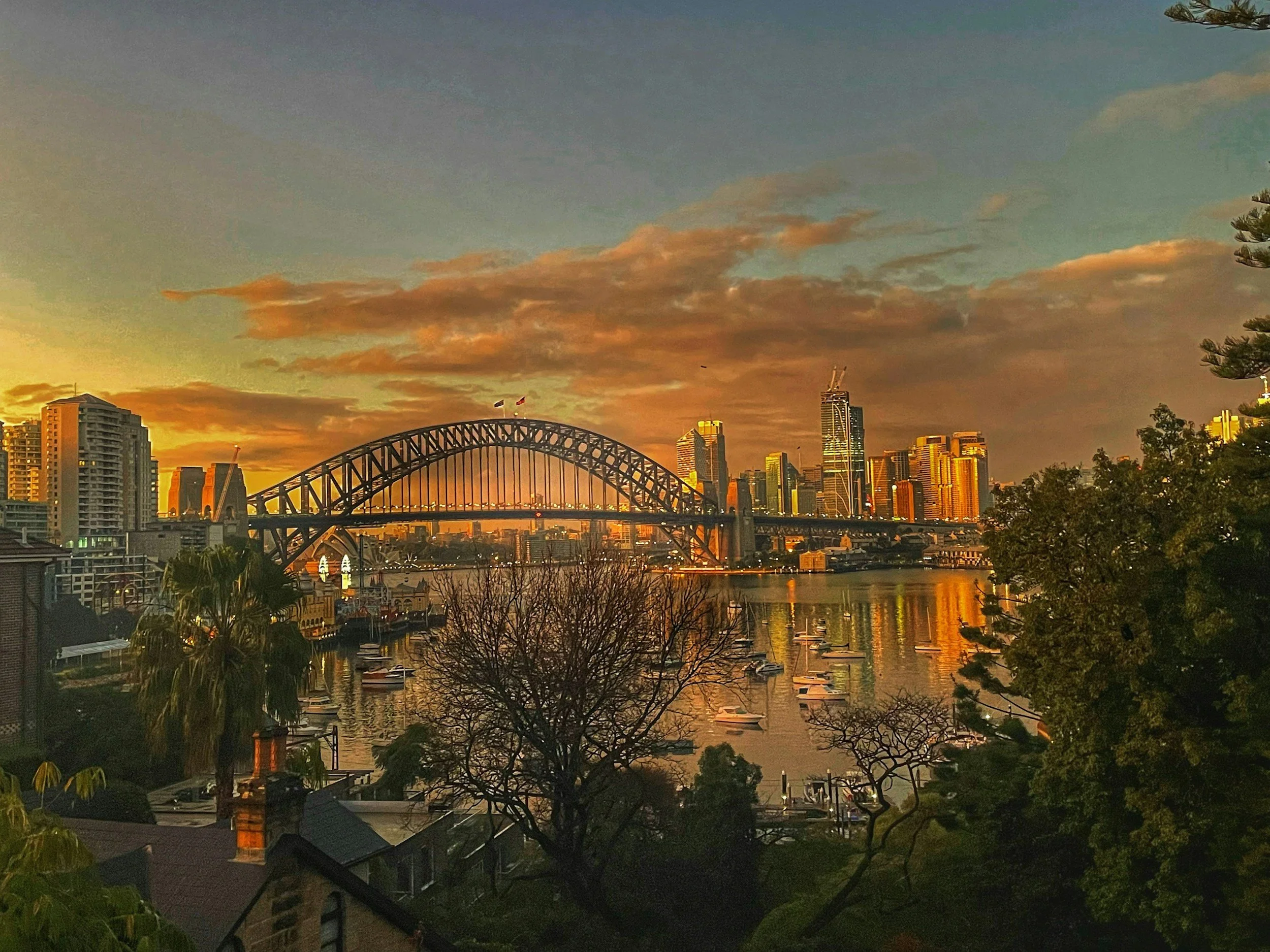 Sunset over Sydney Harbour with the Sydney Harbour Bridge, boats on the water, and city skyscrapers in the background.