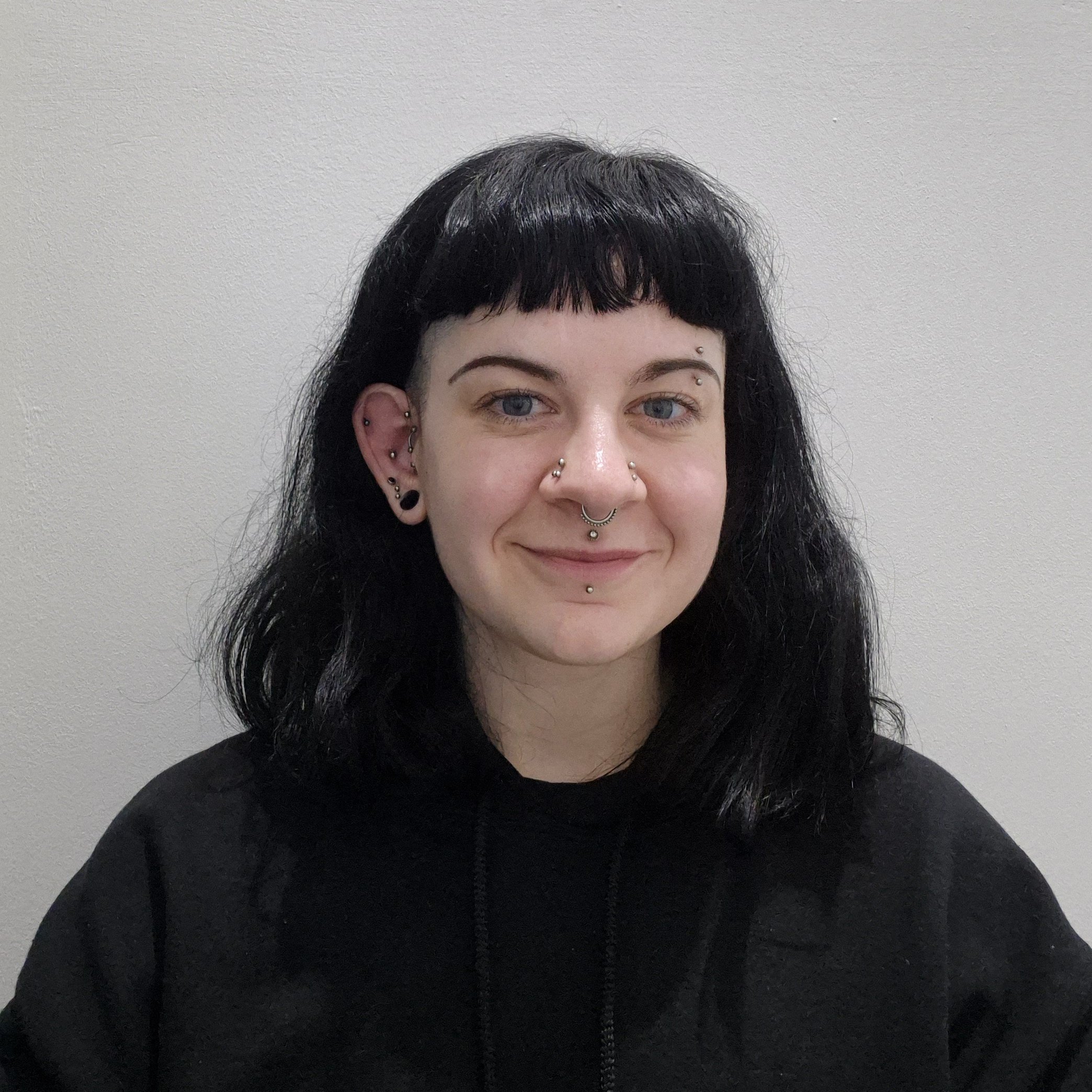 A person with black hair and multiple ear is smiling, facing straight on to the camera. 