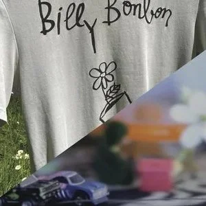 A person wearing a gray shirt with the words 'Billy Bonbon' and a simple flower drawing. The background includes grass and part of an outdoor setting.