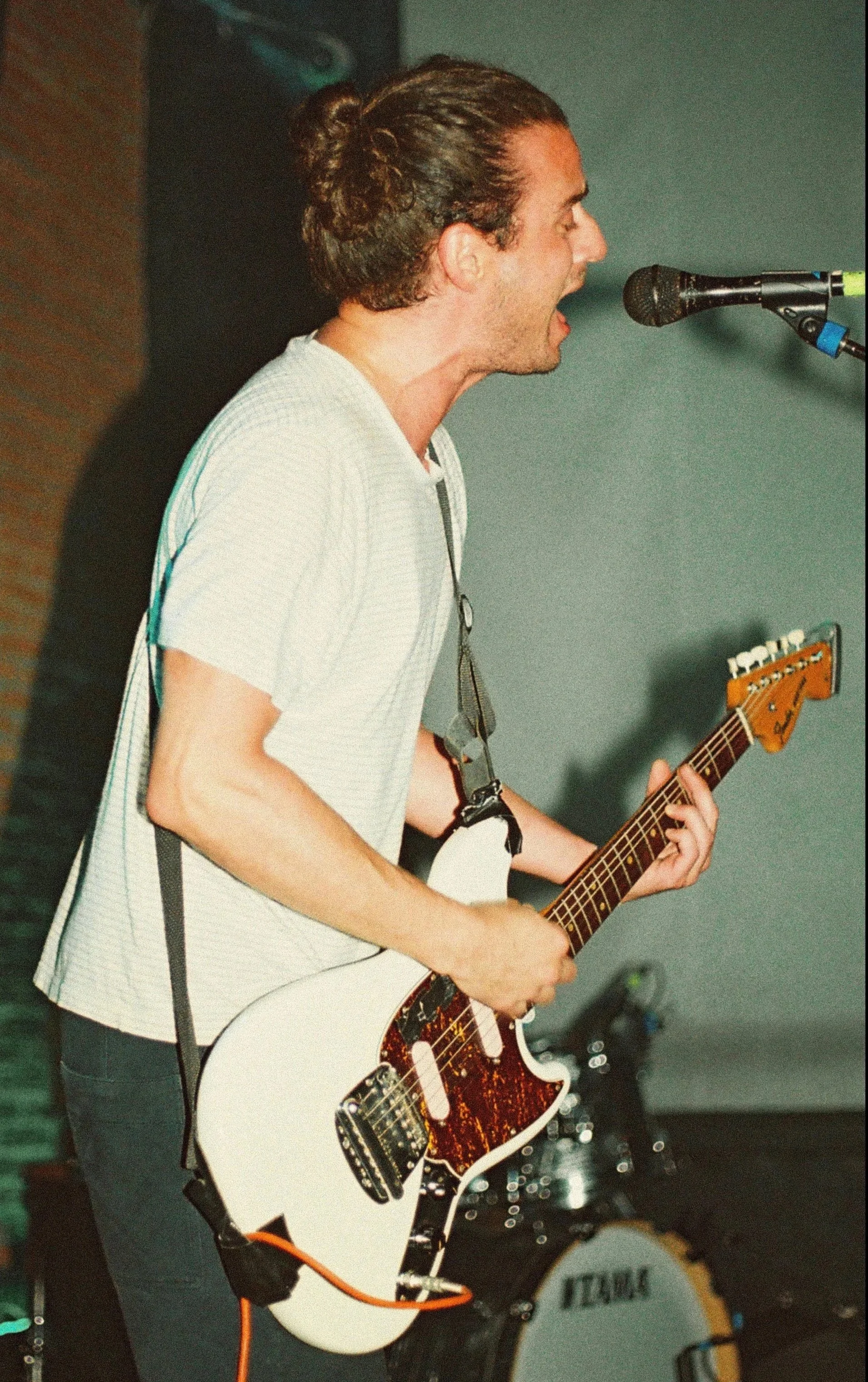 Félix Martinaud of Billy Bonbon with long hair in a bun singing into a microphone while playing an electric guitar.