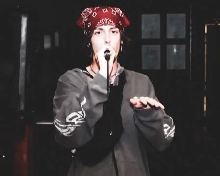 Person wearing a red bandana singing into a microphone on stage.