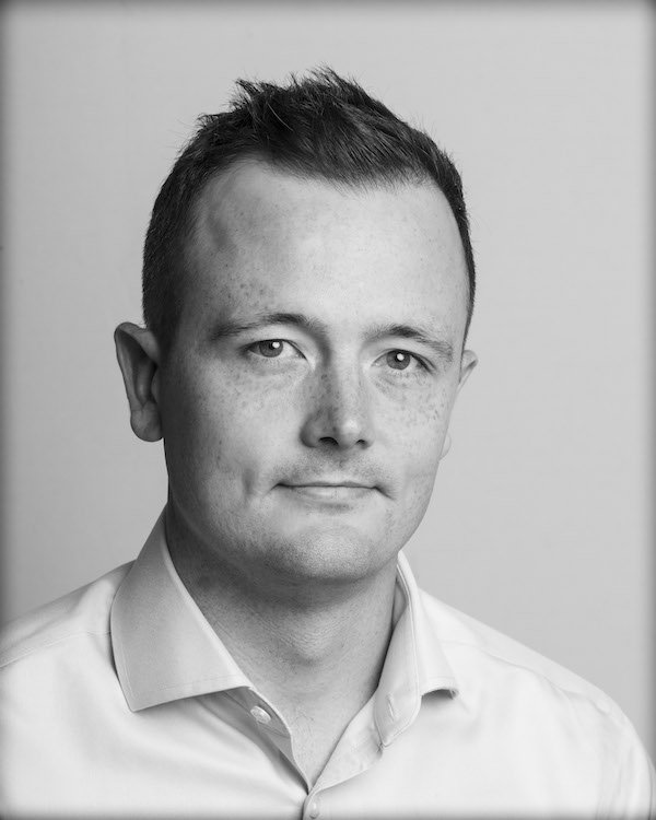 Black and white portrait of a man with short hair, wearing a collared shirt, looking at the camera with a slight smile.