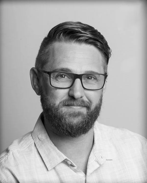 Black and white portrait of a man with short hair, beard, glasses, and wearing a collared shirt.
