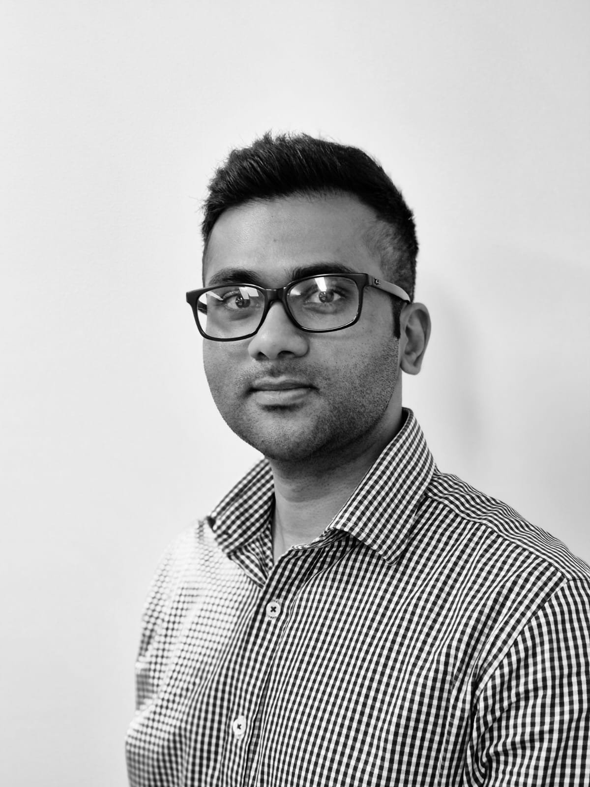 A young man with short hair, wearing a checkered collared shirt, facing the camera with a slight smile.