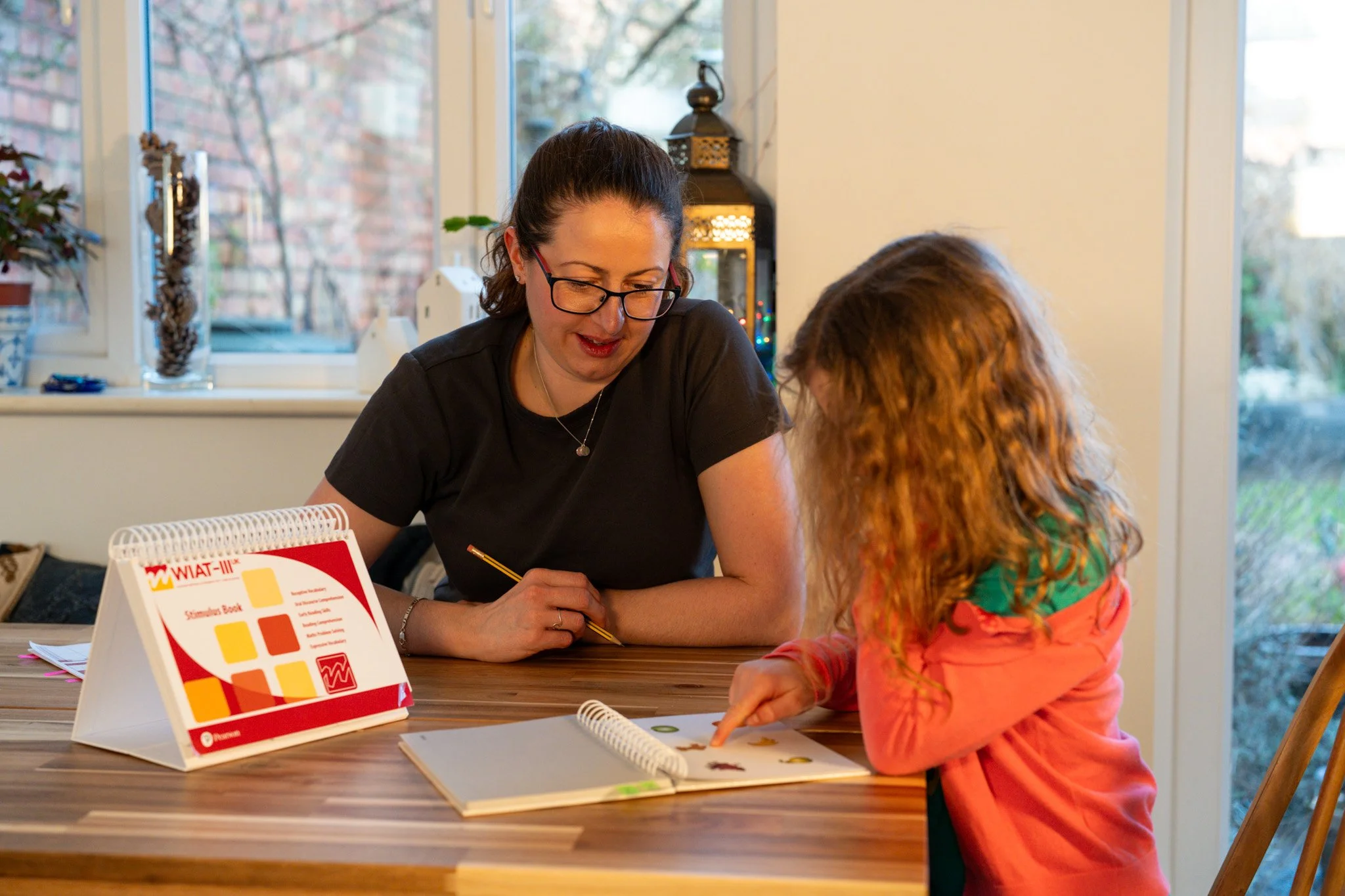 A woman and a child sit at a table and look at a series of pictures which the child points to.