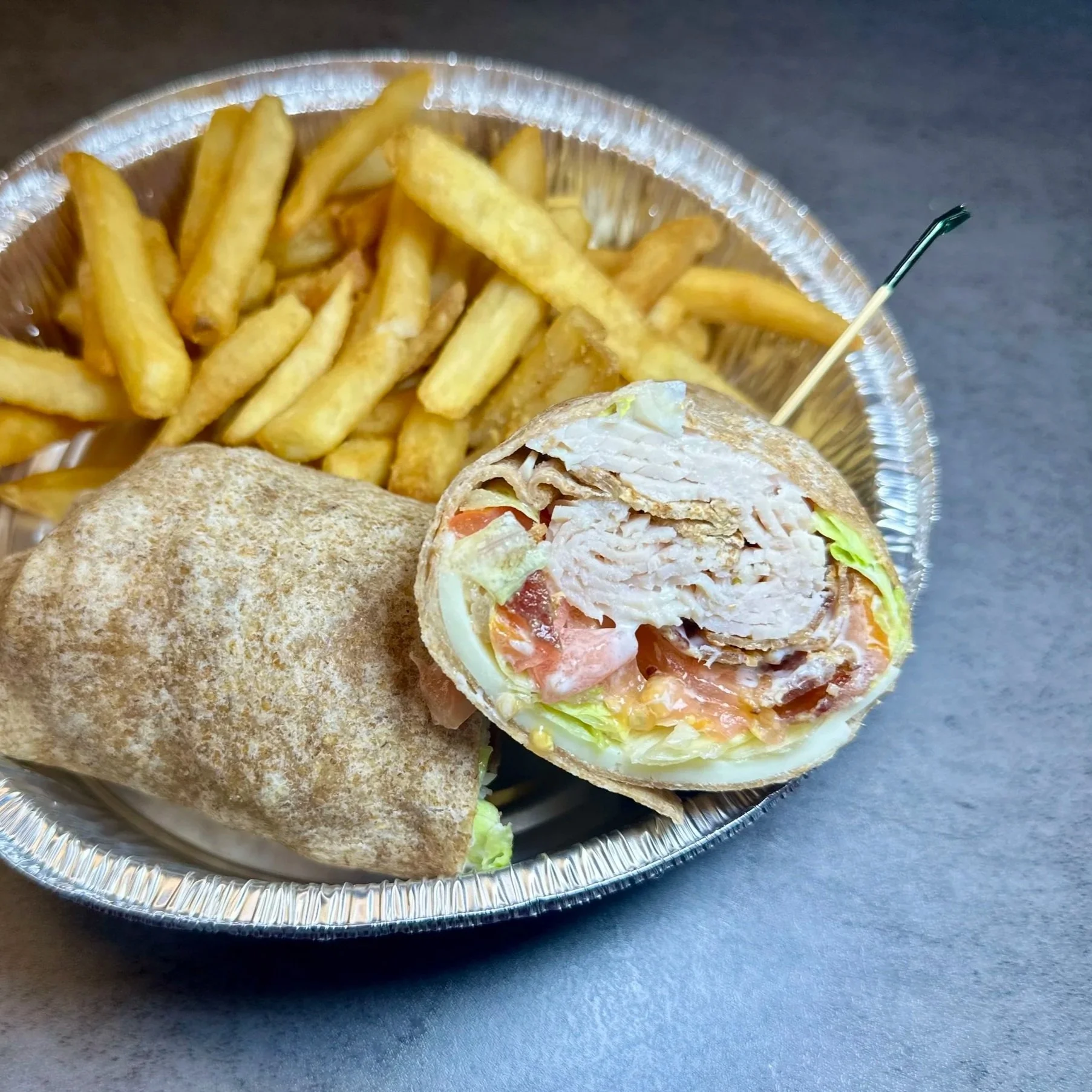 A foil container with French fries and a chicken wrap cut in half showing lettuce, tomato, and chicken inside.