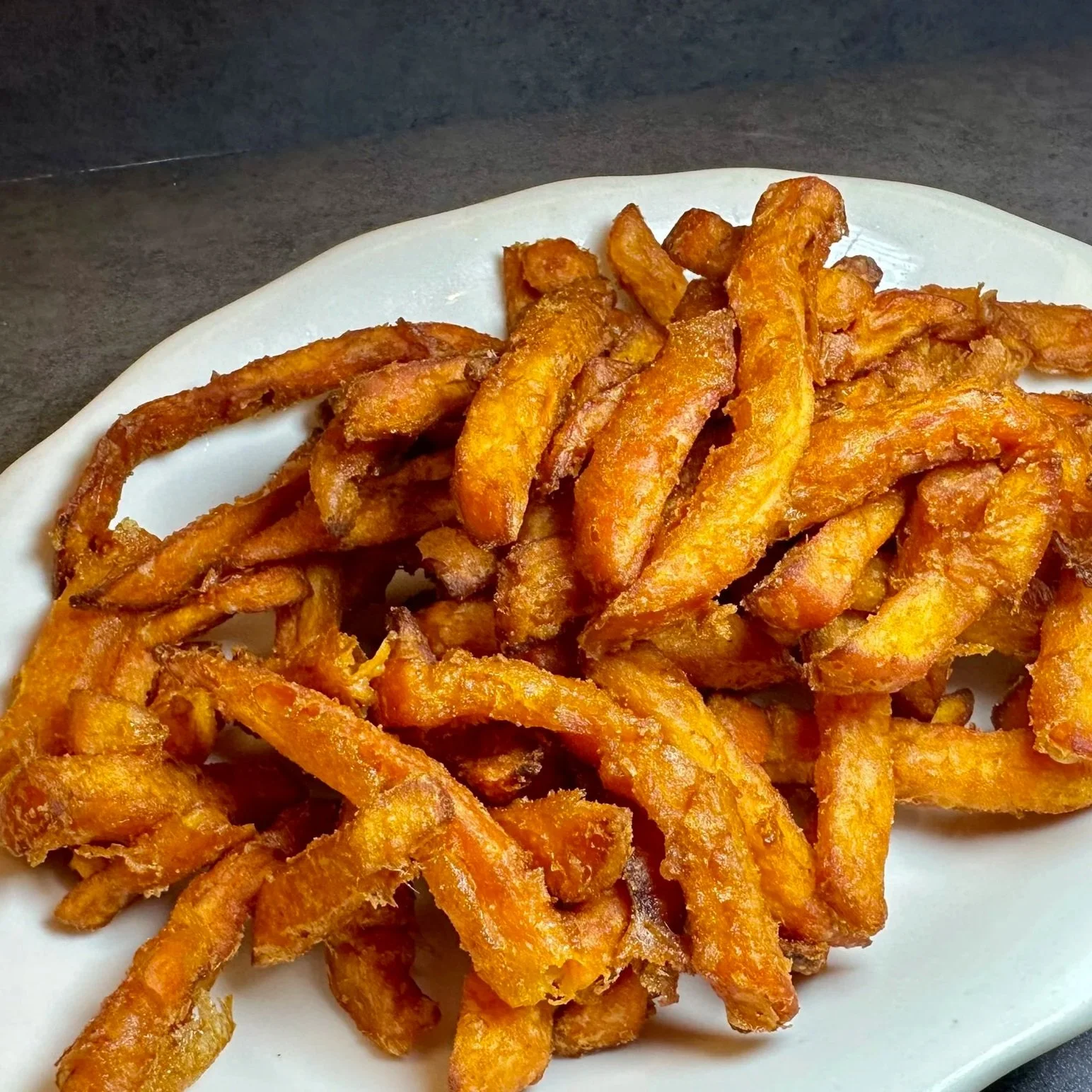A white plate filled with crispy, golden-brown fried potato fries.