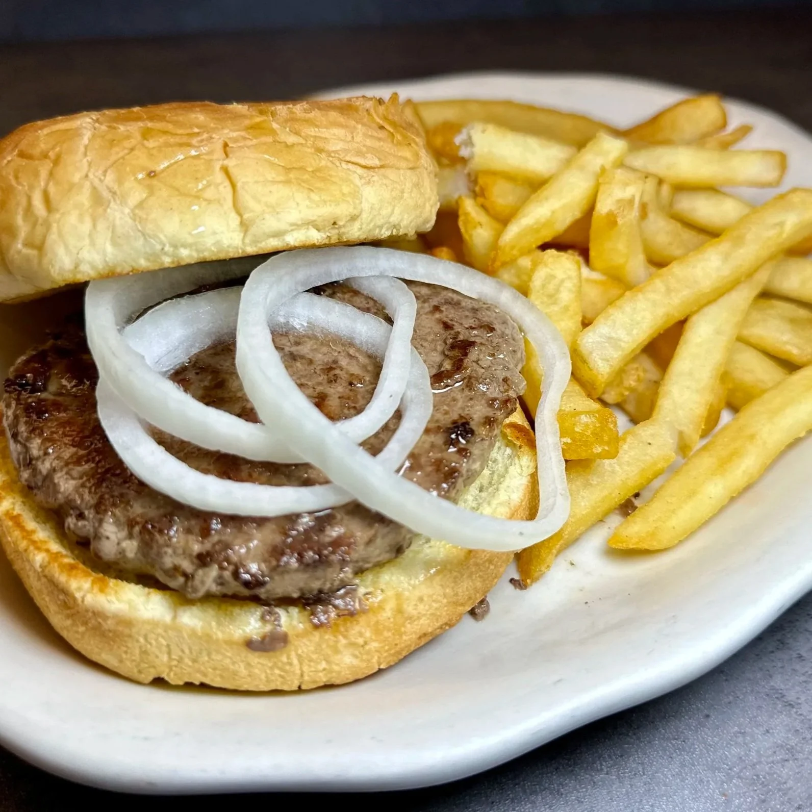 Hamburger with onion rings and French fries on a white plate.
