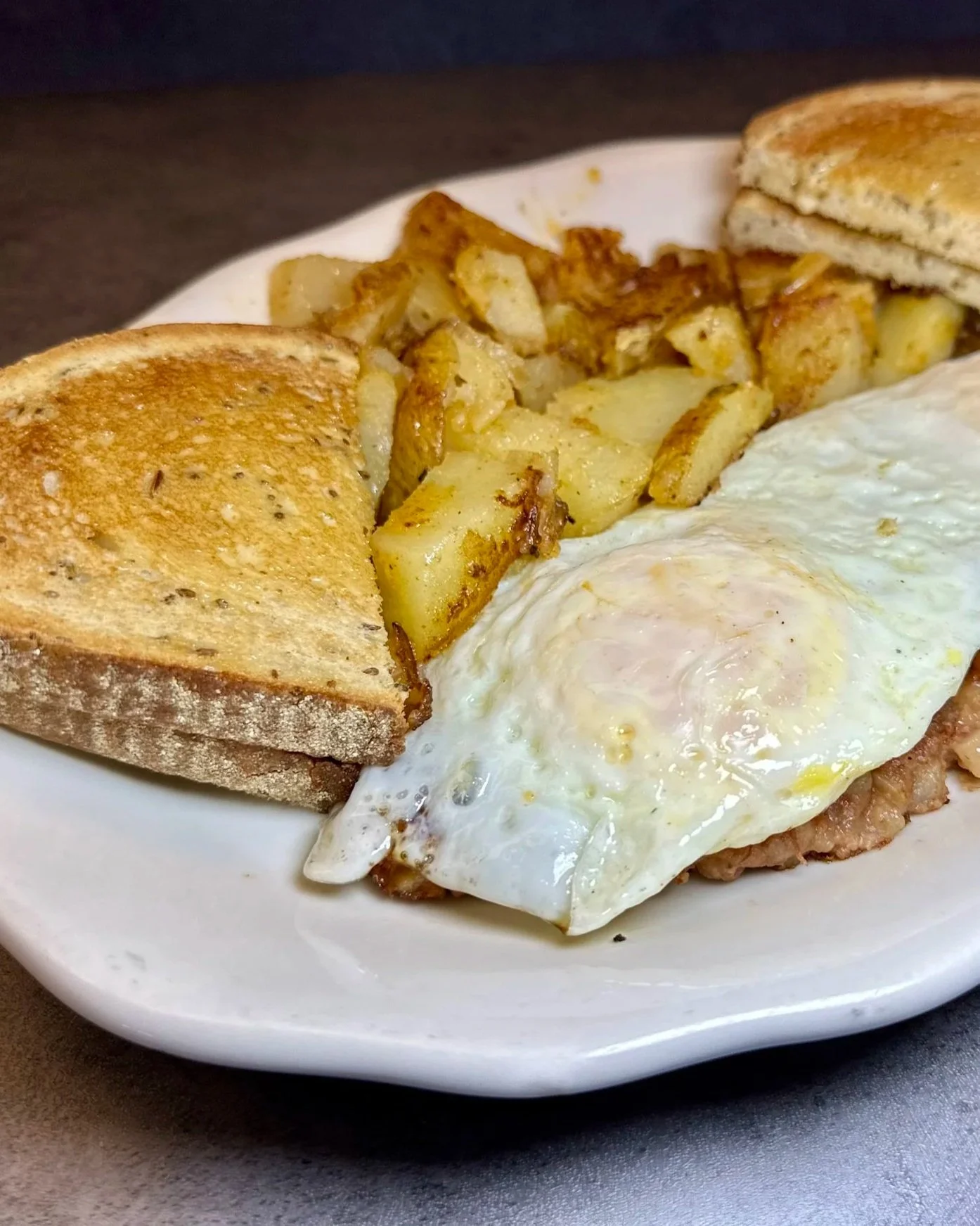 Fried egg on fried potatoes with toasted bread on a white plate.