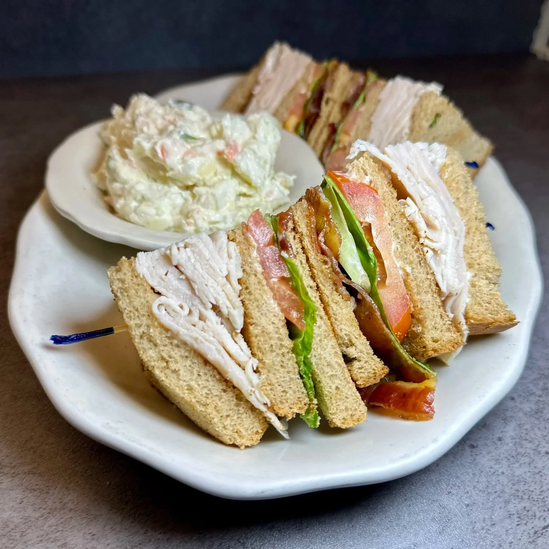 Triangle-cut turkey and vegetable sandwiches on a white plate with potato salad.