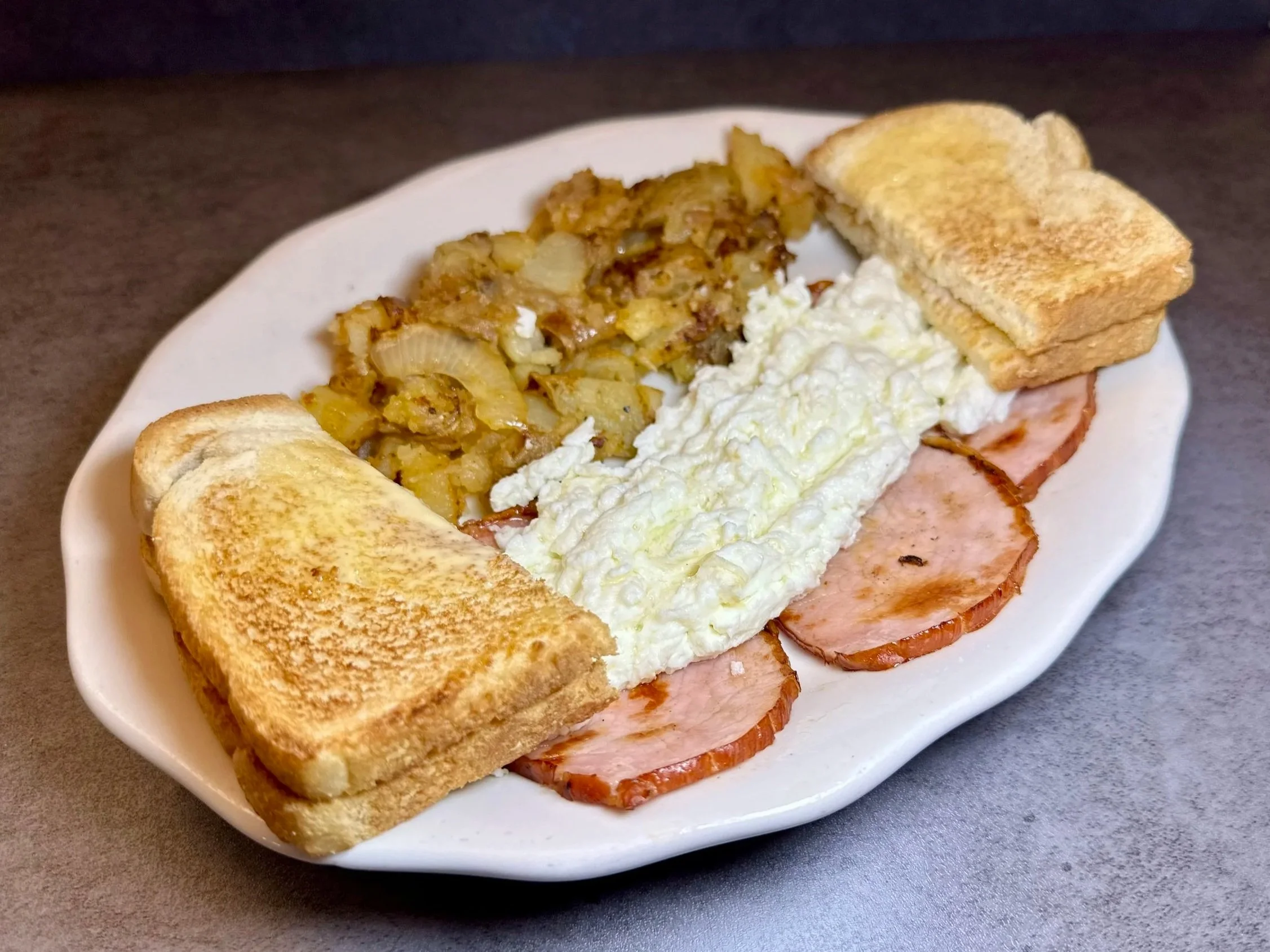 Plate with fried eggs, sliced ham, potato hash browns, and toasted bread slices.