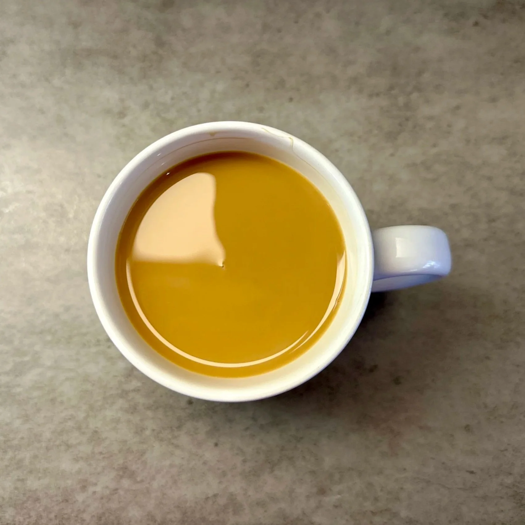 A top-down view of a white mug filled with coffee or tea on a gray surface.