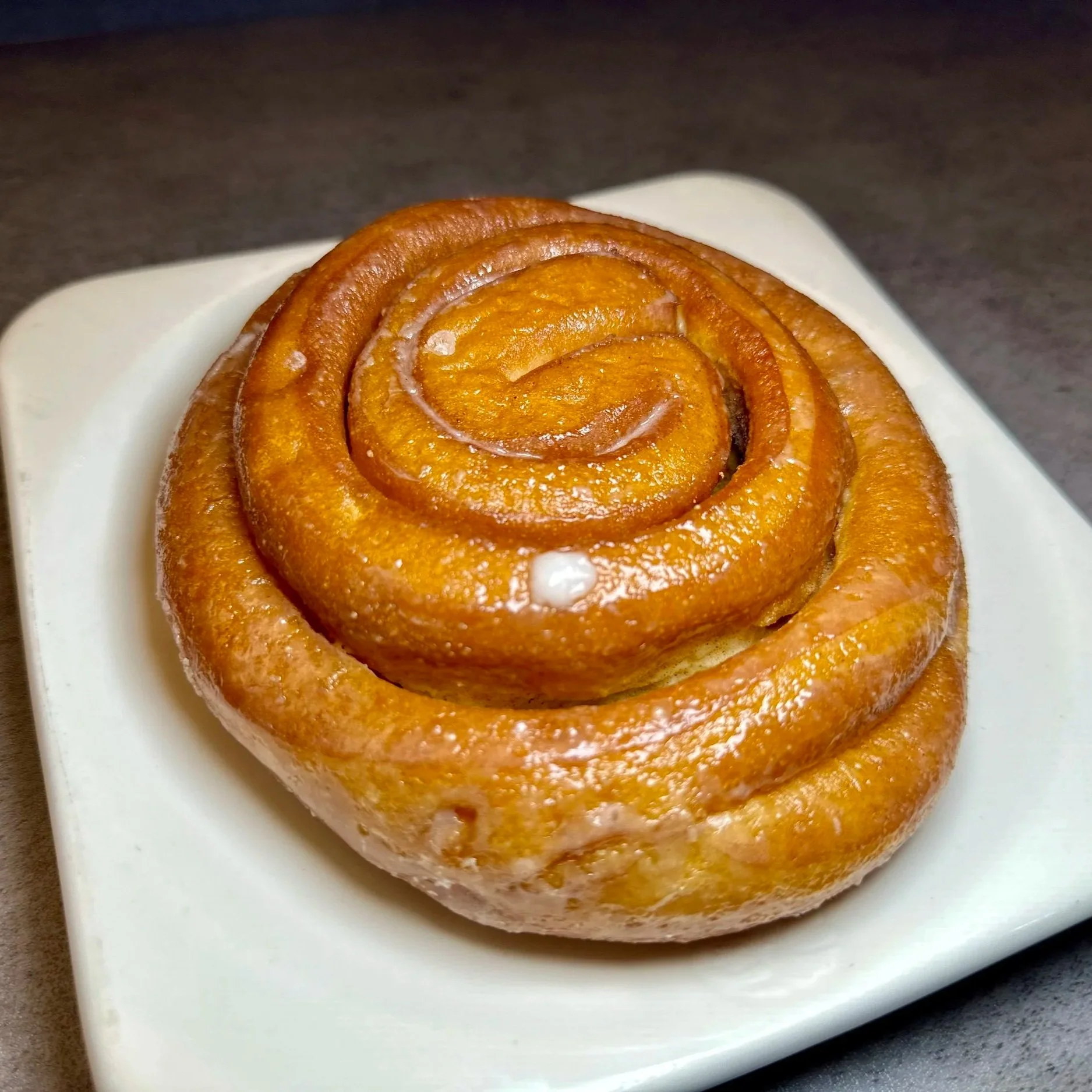 Close-up of a cinnamon roll with a glazed surface on a white plate.