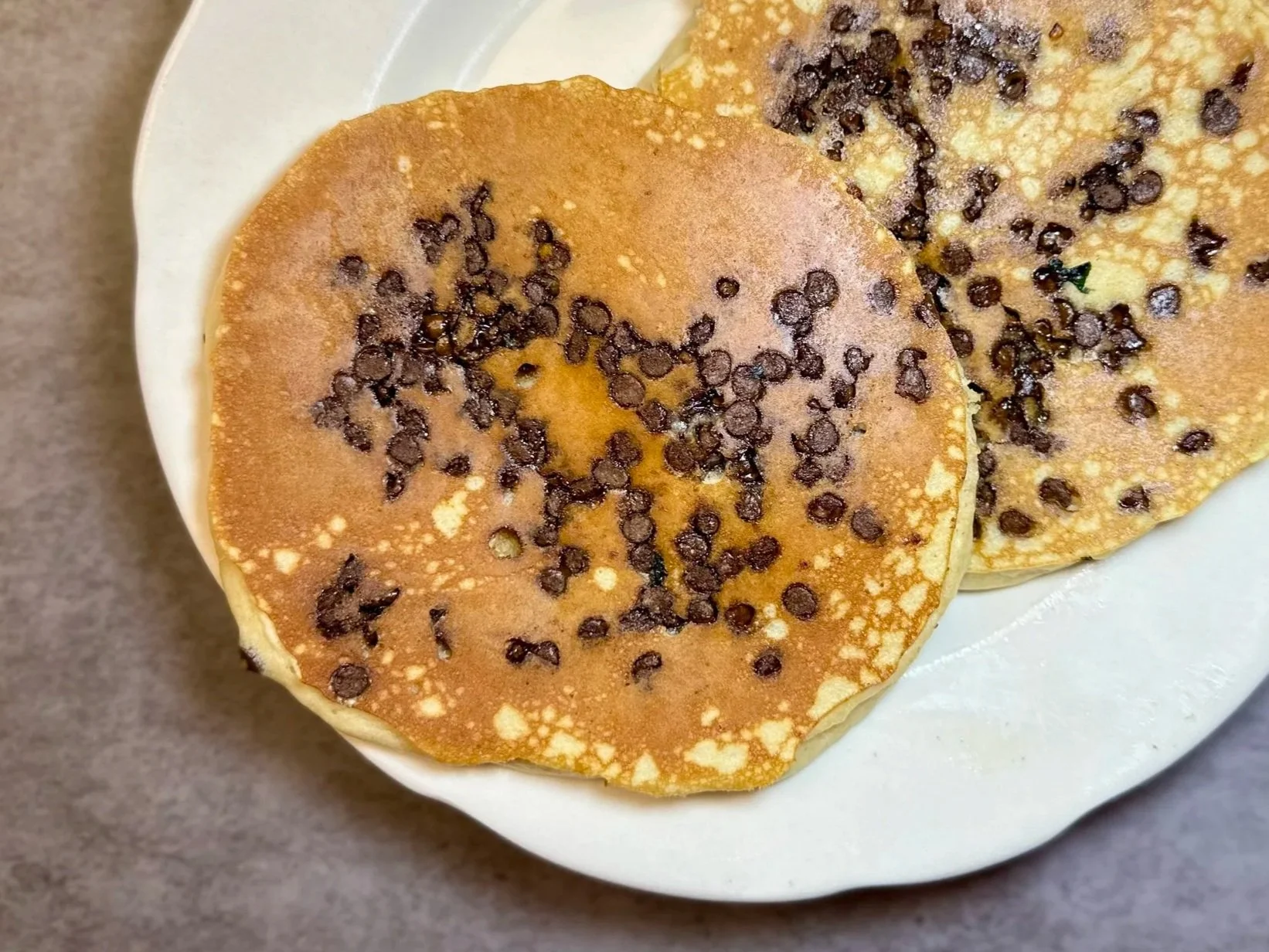 Close-up of two fluffy pancakes topped with chocolate chips on a white plate.