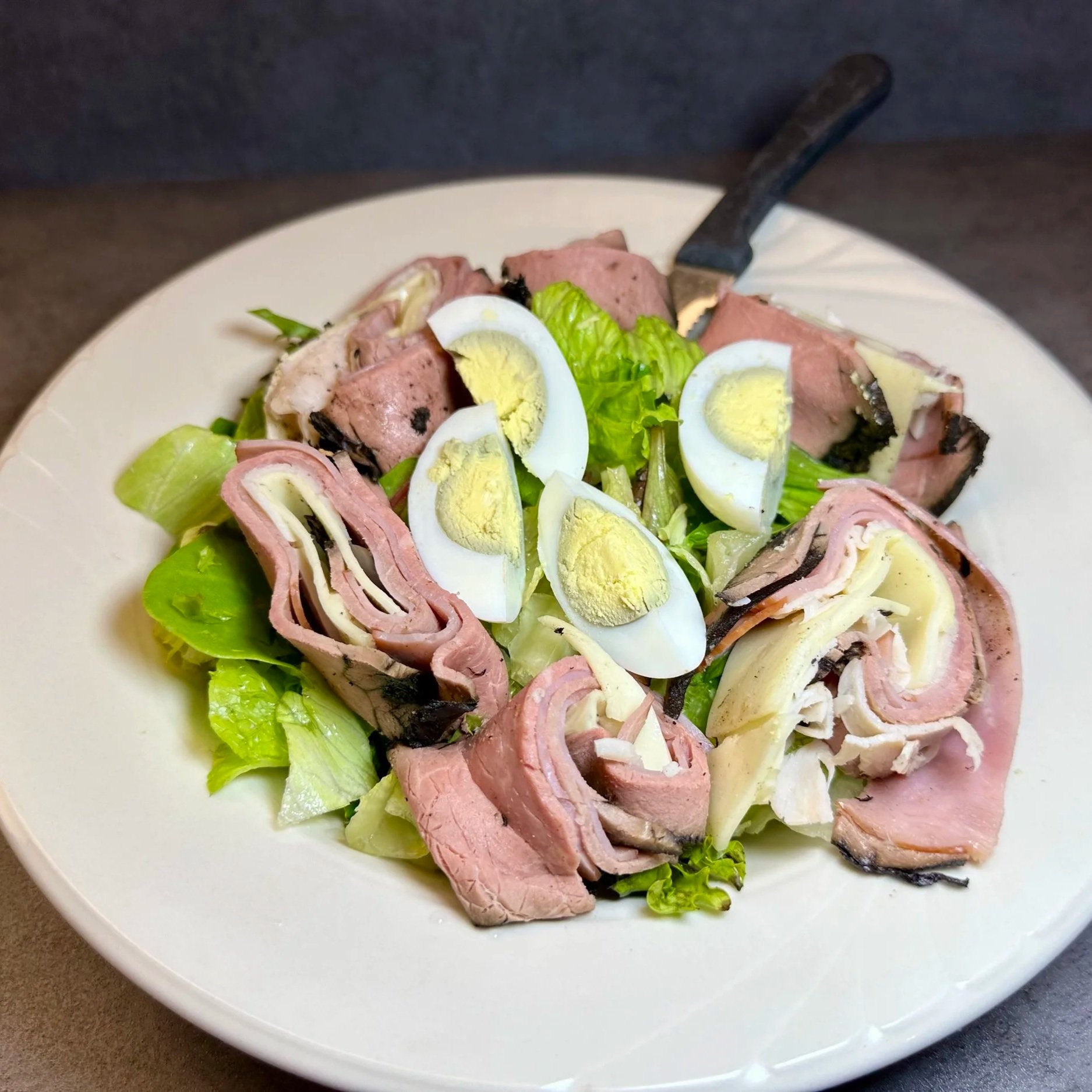 A plate of salad with sliced deli meats, chopped lettuce, and sliced hard-boiled eggs