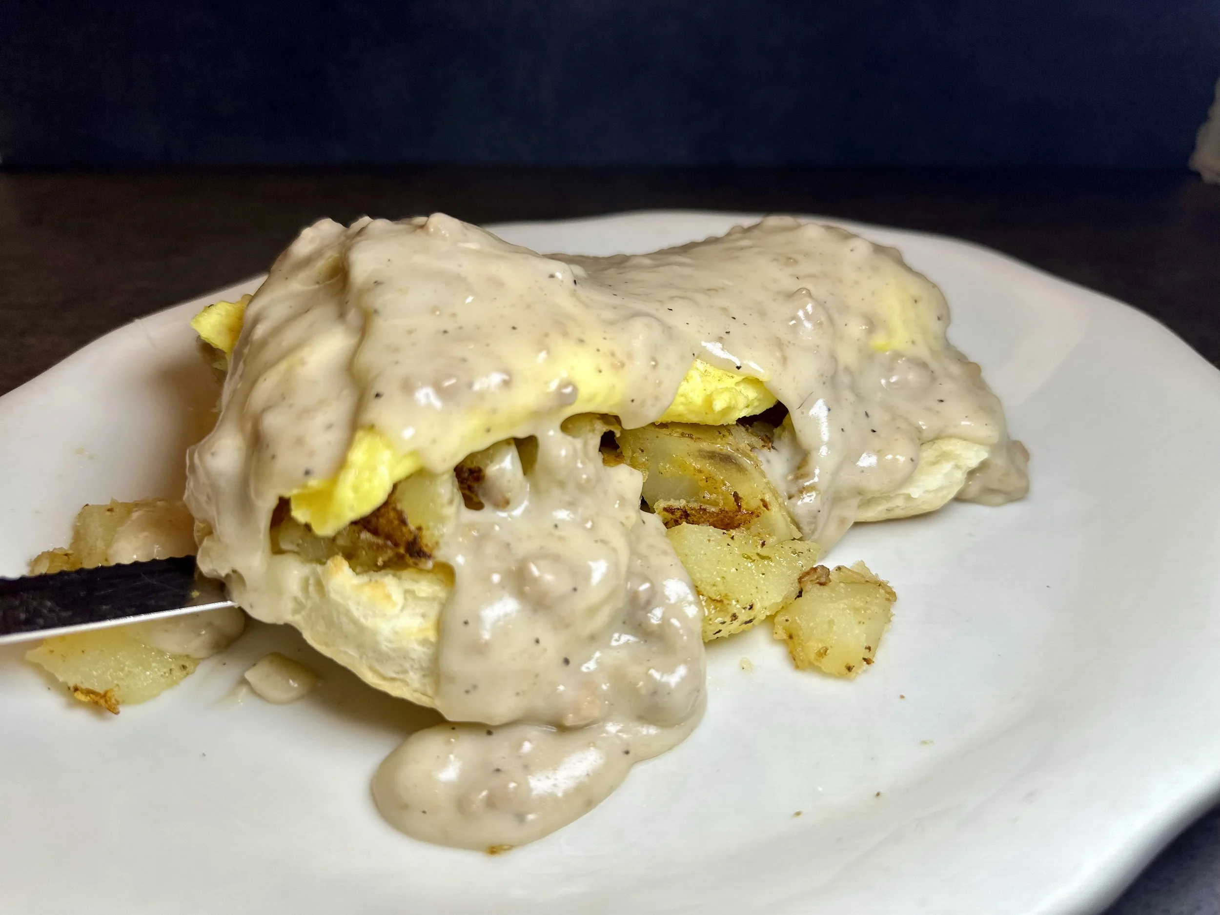 Close-up of a serving of breakfast casserole with eggs, potatoes, and sausage covered in creamy gravy on a white plate.