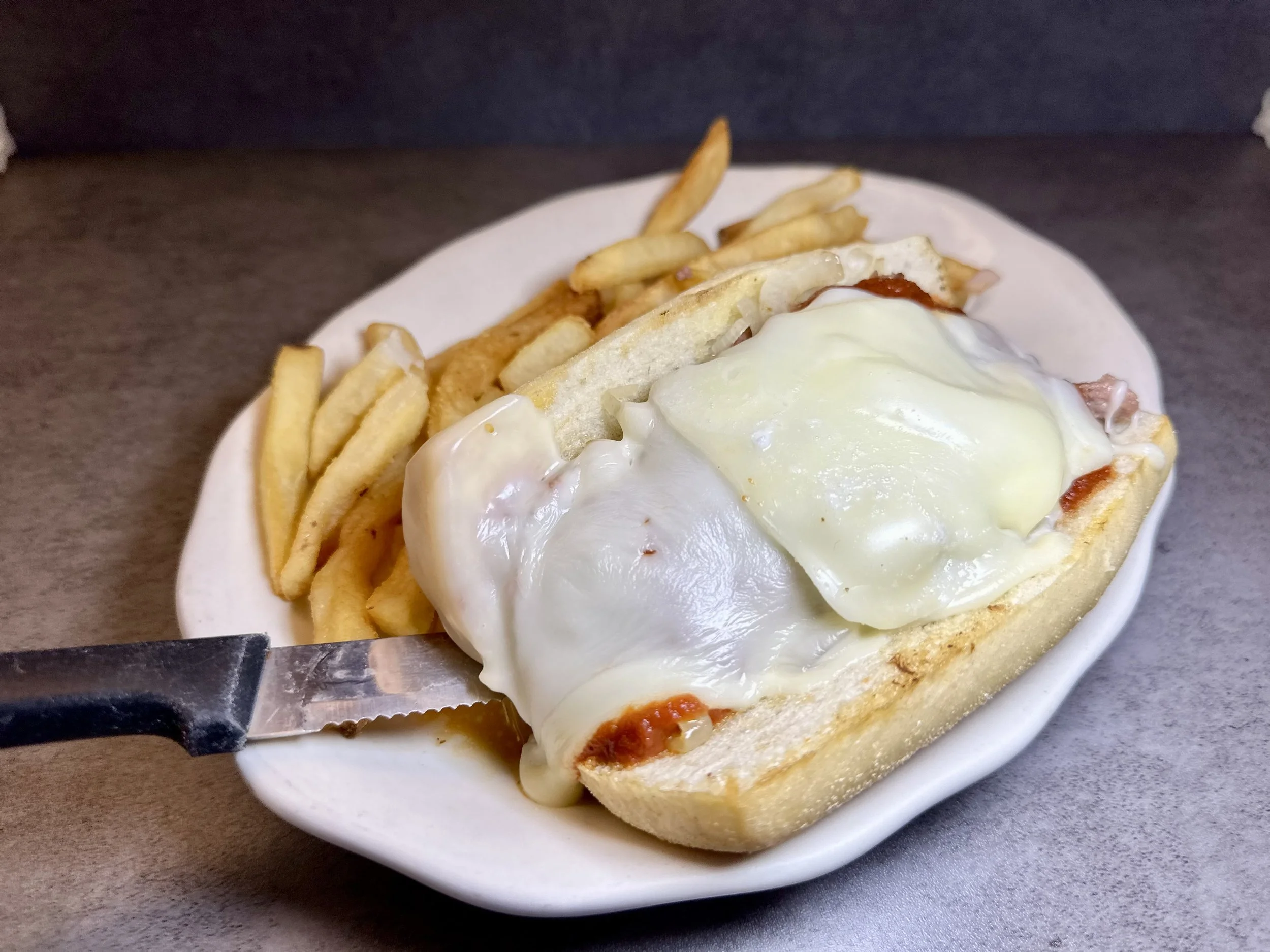 Open-faced sandwich with melted cheese, eggs, and tomato slices, served with French fries on a white plate