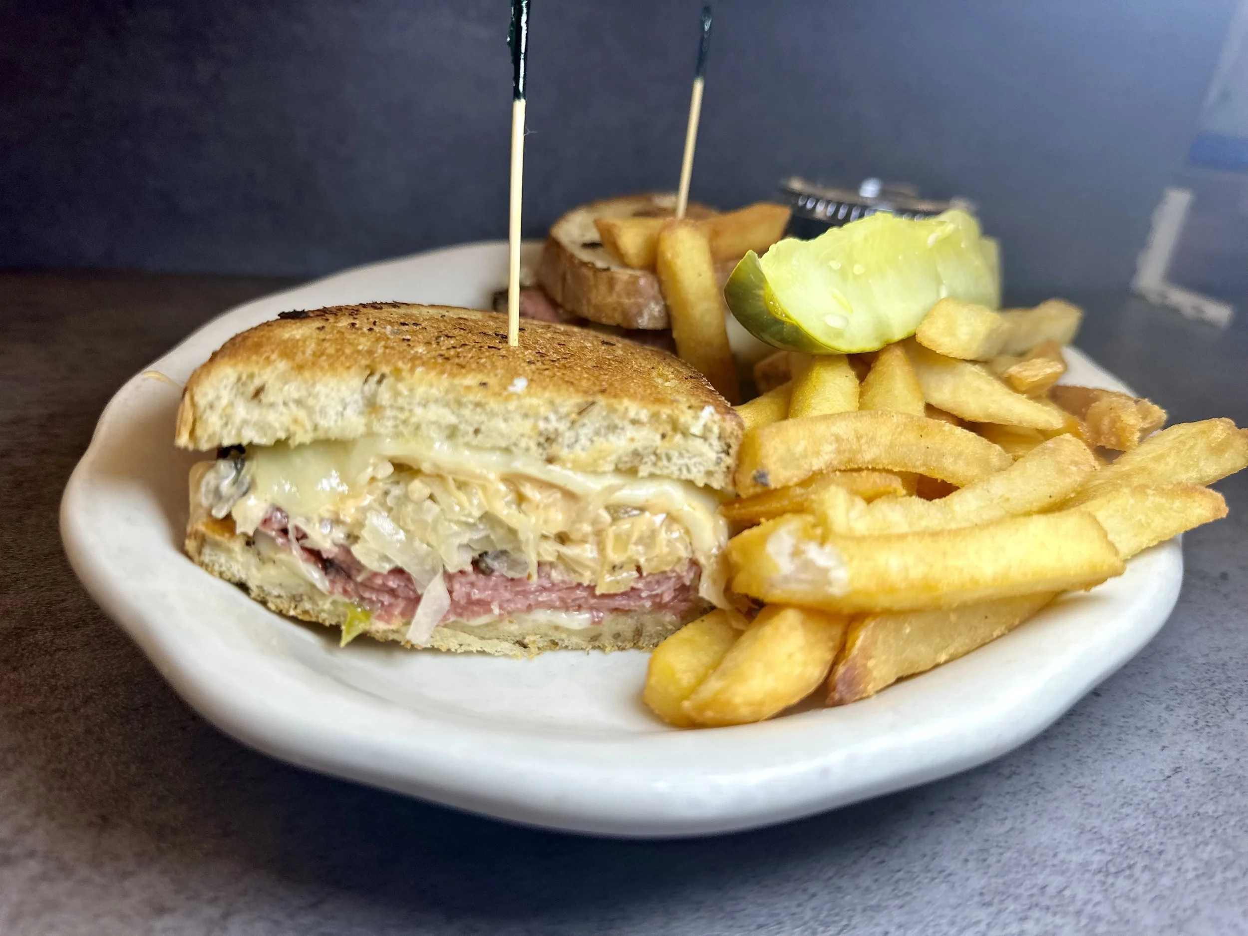 Half-eaten cheeseburger with pickles, French fries, and a pickle slice on a white plate.