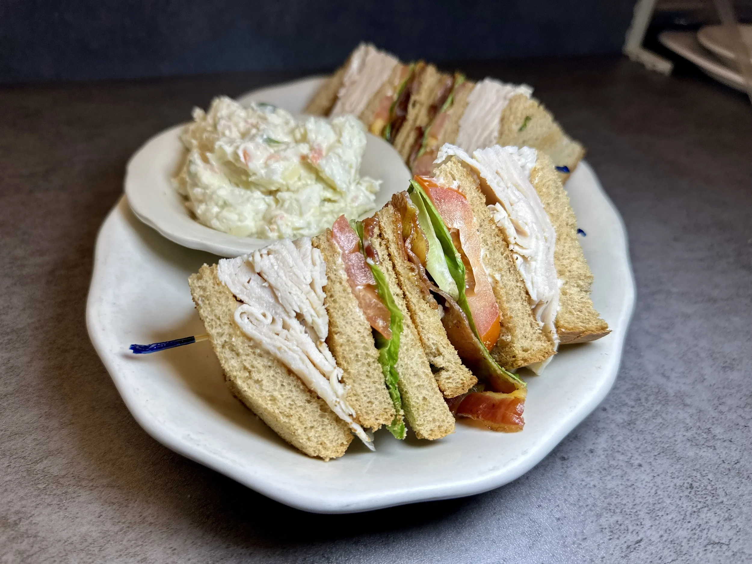 Plate with chicken salad sandwiches, lettuce, tomato, and potato salad.