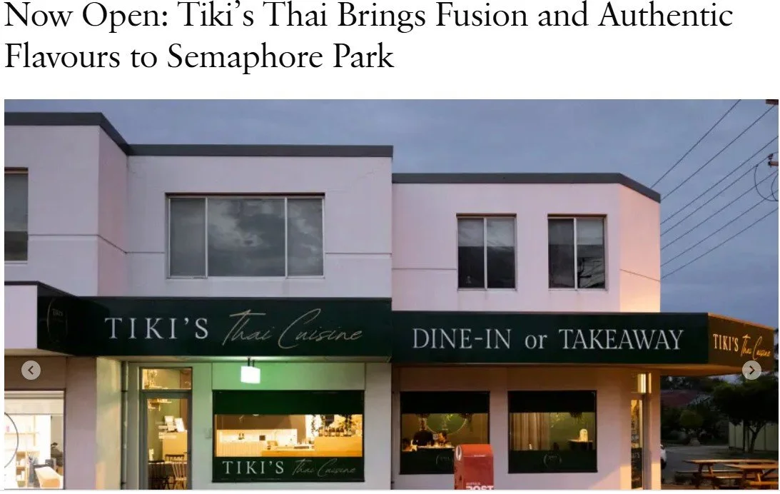 Exterior of a modern two-story building with a green sign reading 'TIKI'S Thai Cuisine DINE-IN or TAKEAWAY'. The building has a white facade with large windows, and there are a couple of outdoor tables and chairs visible.