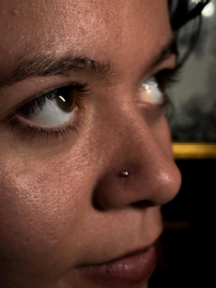 Close-up of a person's face showing brown eyes, eyebrow, nose with a small nose ring, and lips.