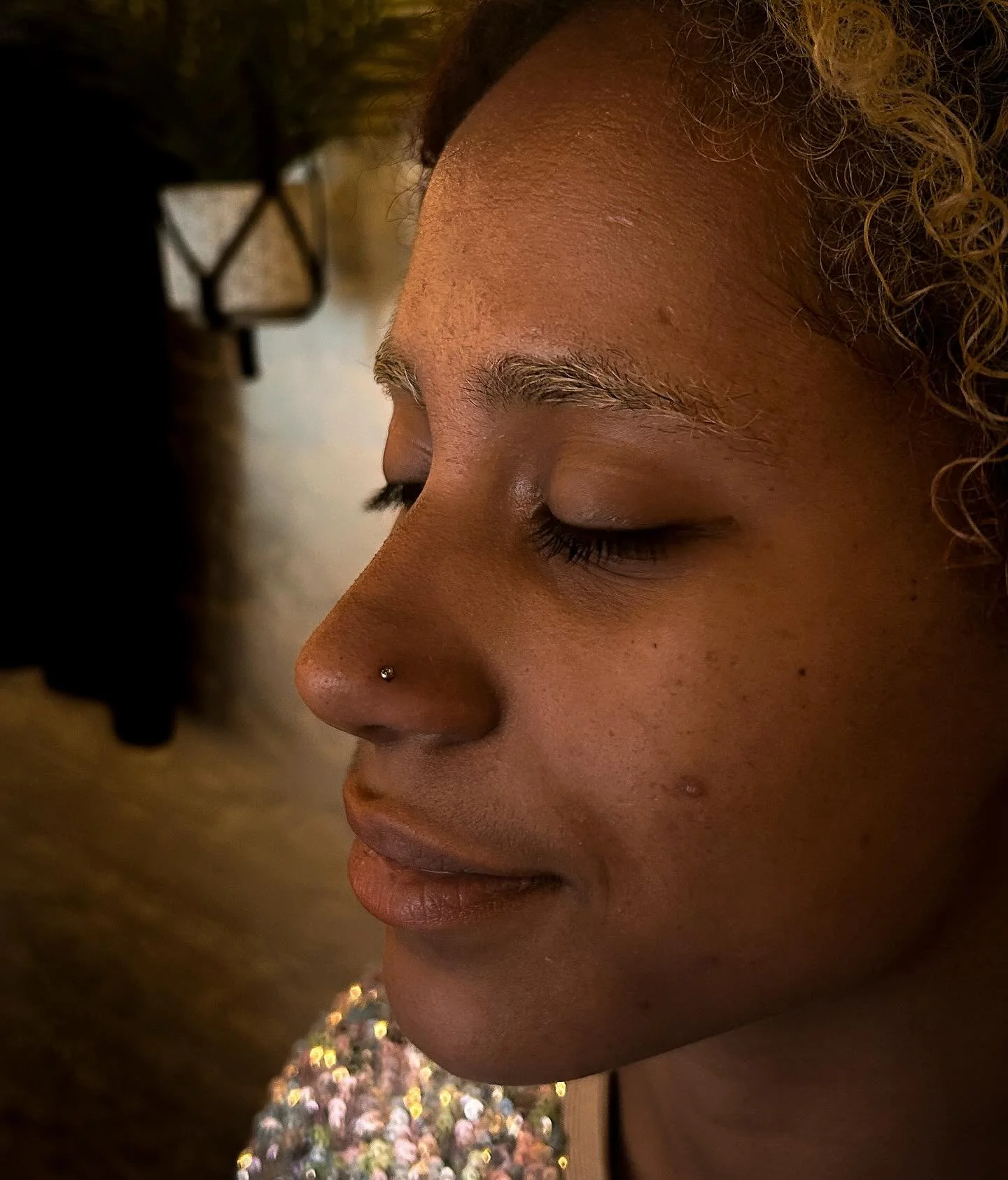 Close-up of a woman's face with closed eyes, wearing a nose ring, and curly hair, in a peaceful expression.