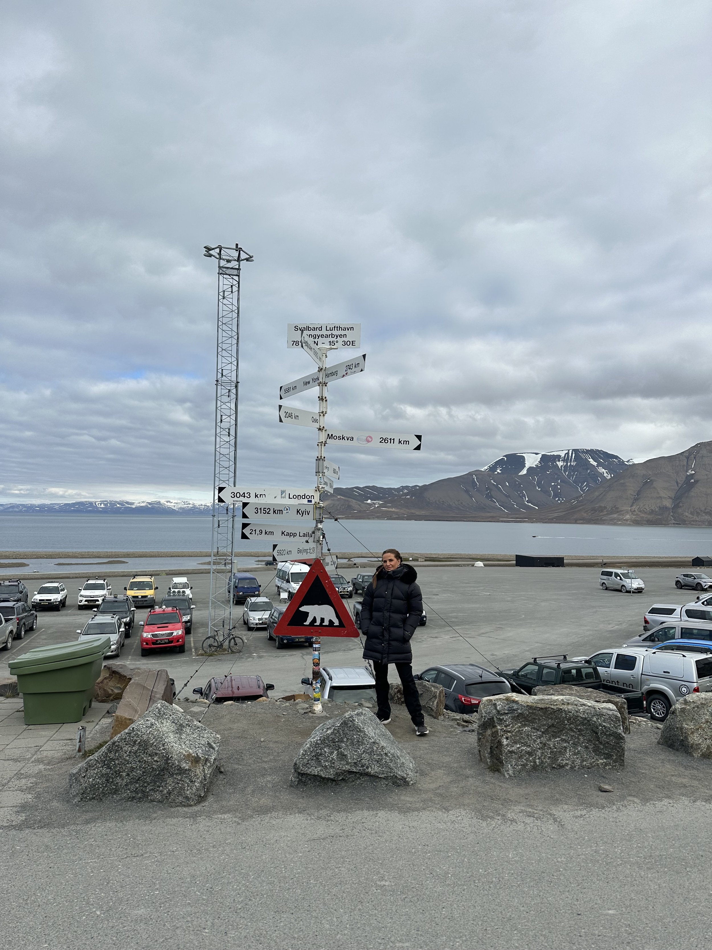 Woman standing in front of polar bear warning sign in Svalbard showing distances to various locations.