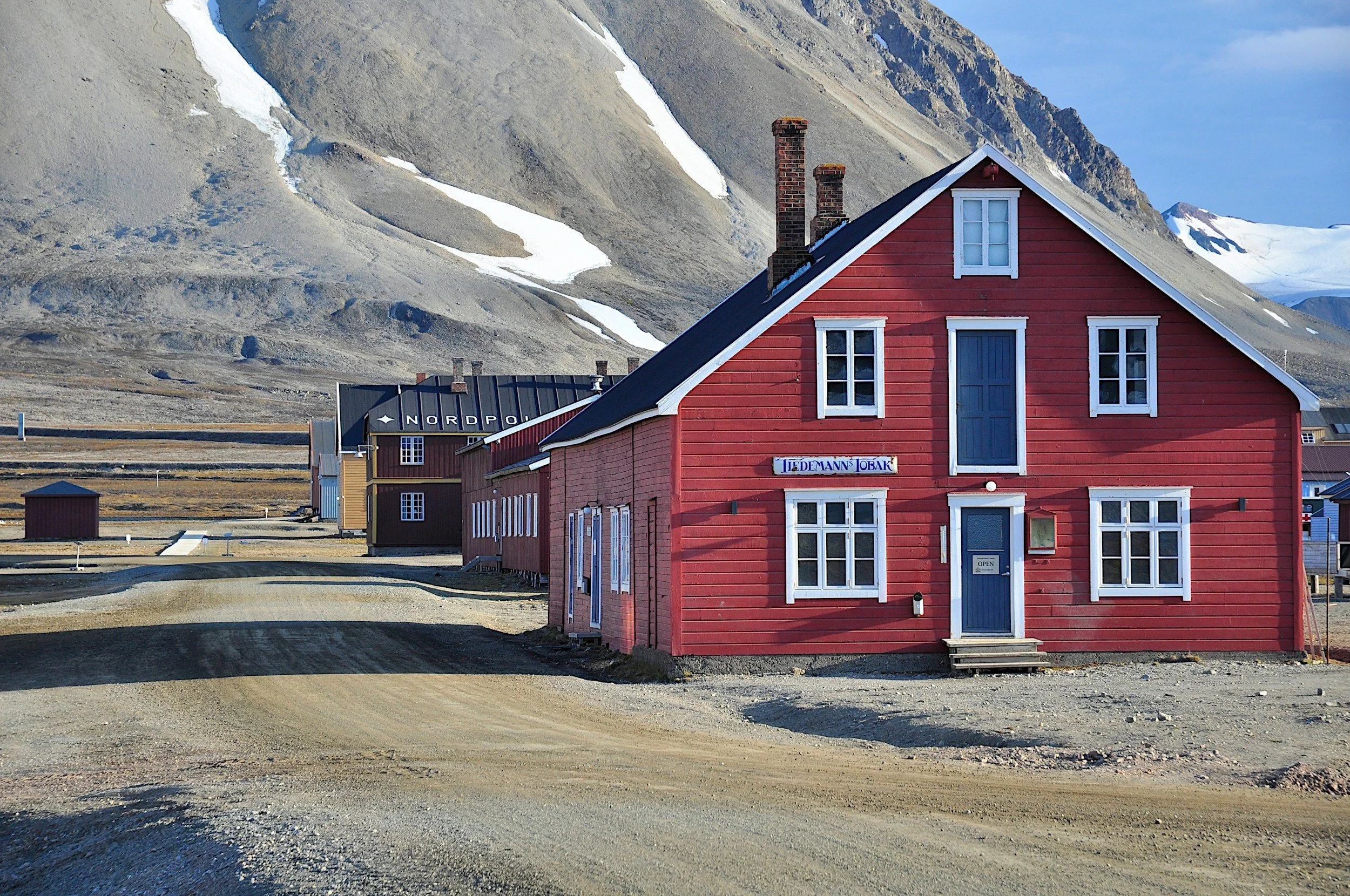 Traditional red wooden house in Longyearbyen, Svalbard, standing against a backdrop of bare mountains and Arctic tundra.