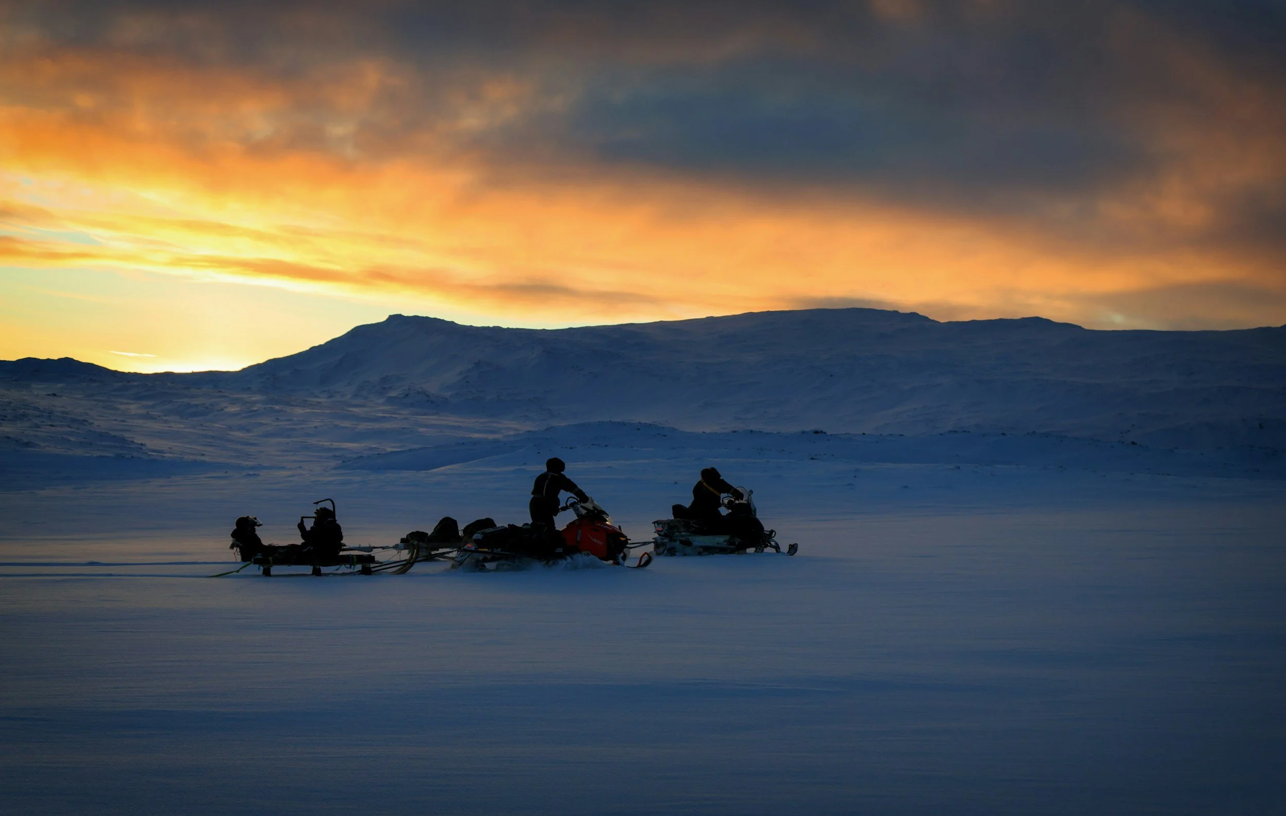 Snowmobile group crossing a snowy Arctic plateau in Svalbard during a colourful polar twilight.
