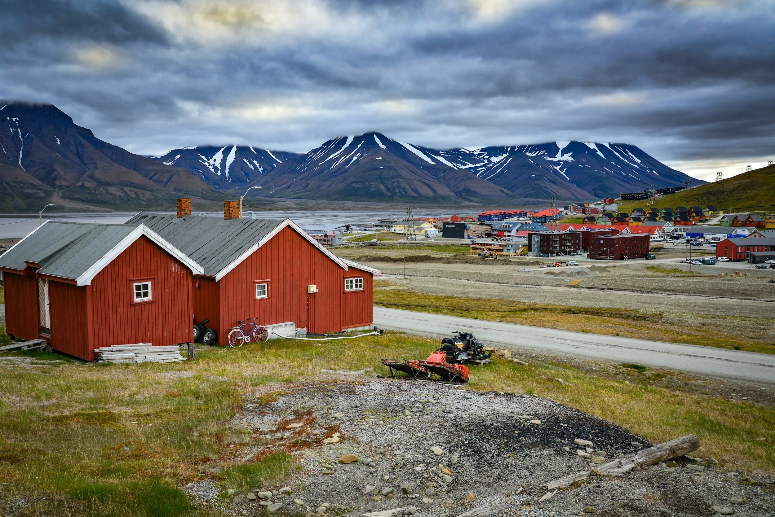 Summer view in Longyearbyen with vibrant buildings, bare tundra landscape and dramatic mountains partly covered in snow.