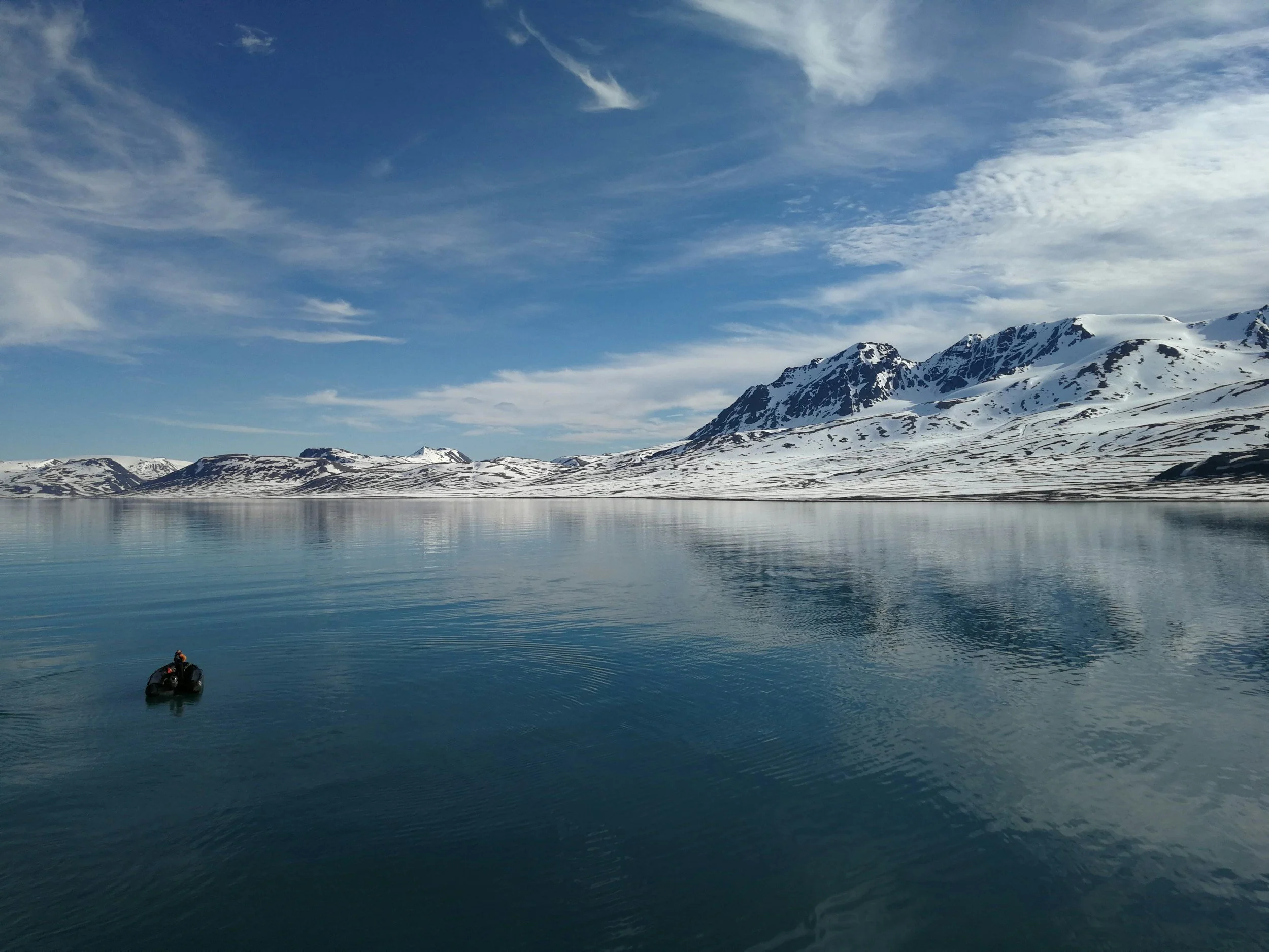 Small boat on calm turquiose water in Svalbard, surrounded by snow-covered mountains and bright summer skies.