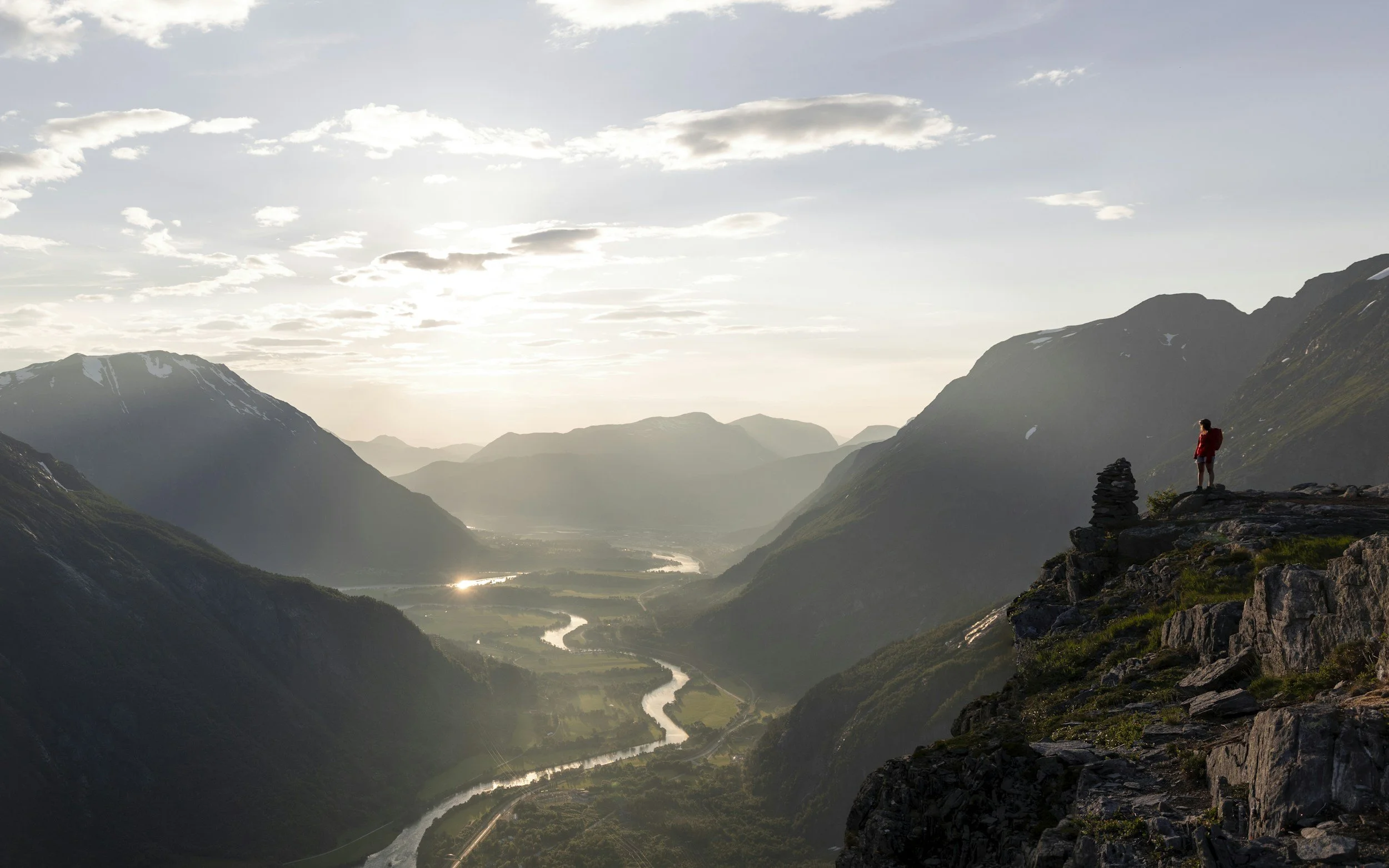 Hiker standing on a mountain viewpoint in Norway overlooking dramatic peaks valleys and winding rivers showcasing Norway hiking landscapes and spectacular mountain scenery