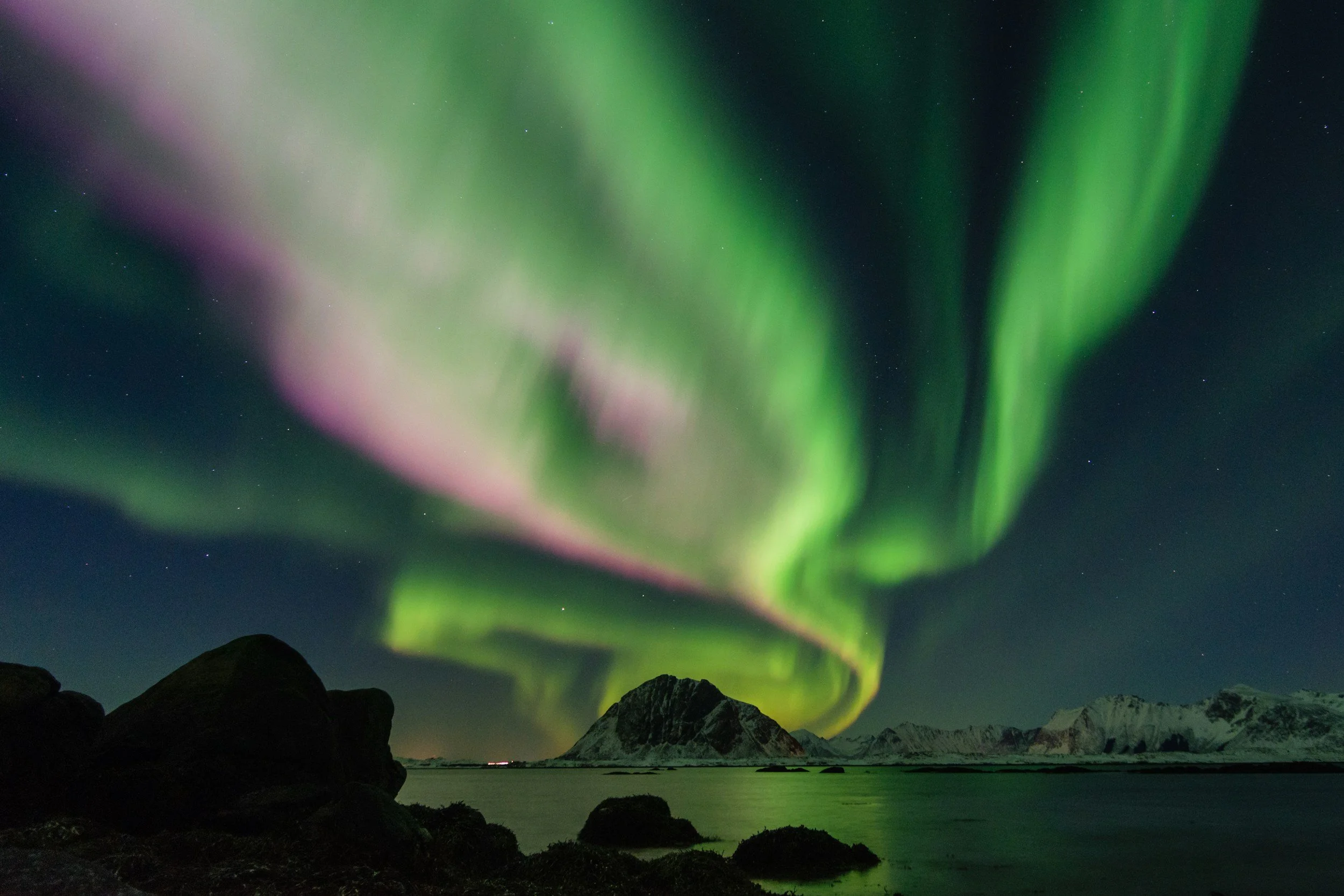 Northern lights glowing in green and pink over mountains and coastline in northern Norway showing how Norway is one of the best places in the world to see the aurora borealis