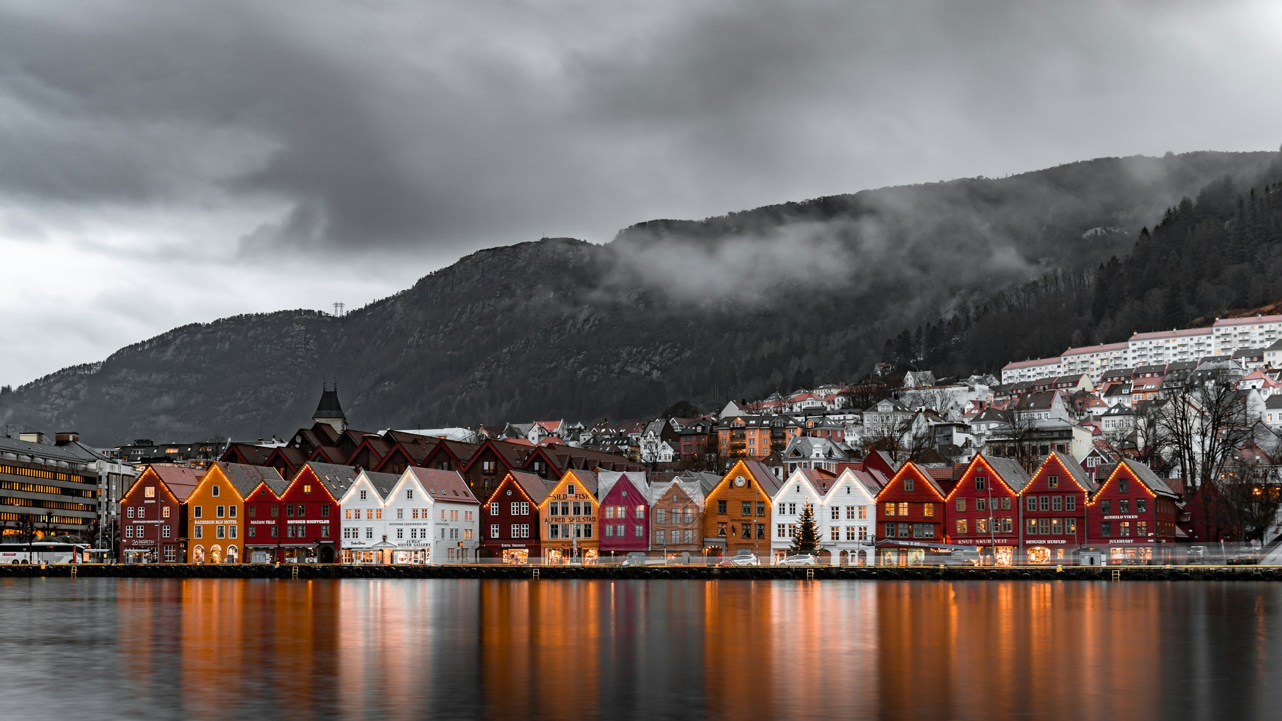Colourful Bryggen wooden houses reflected in the harbour in Bergen Norway with mountains and low clouds showing classic west coast scenery and a popular year round travel destination