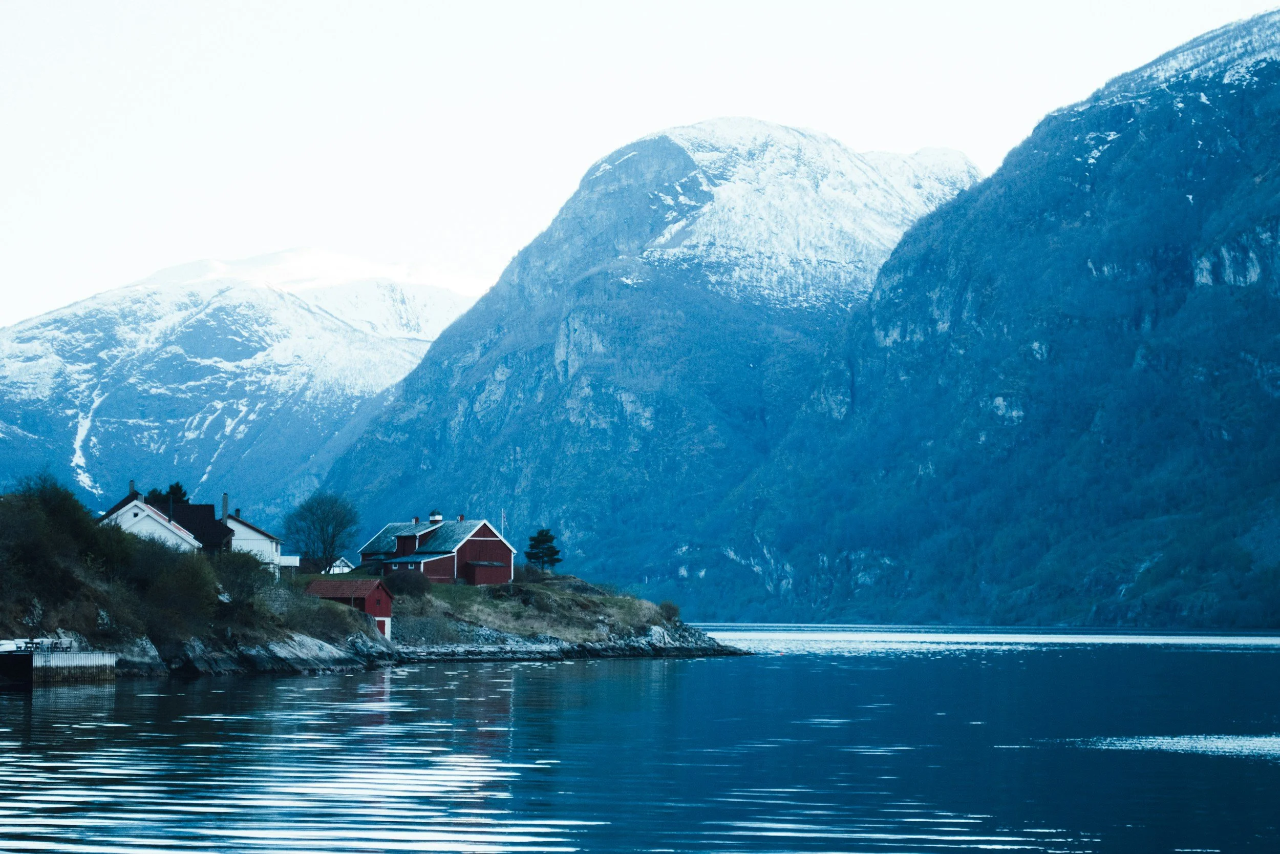 Norwegian fjord with calm reflective water snow-capped mountains and traditional red coastal houses showcasing classic Norway fjord scenery and travel