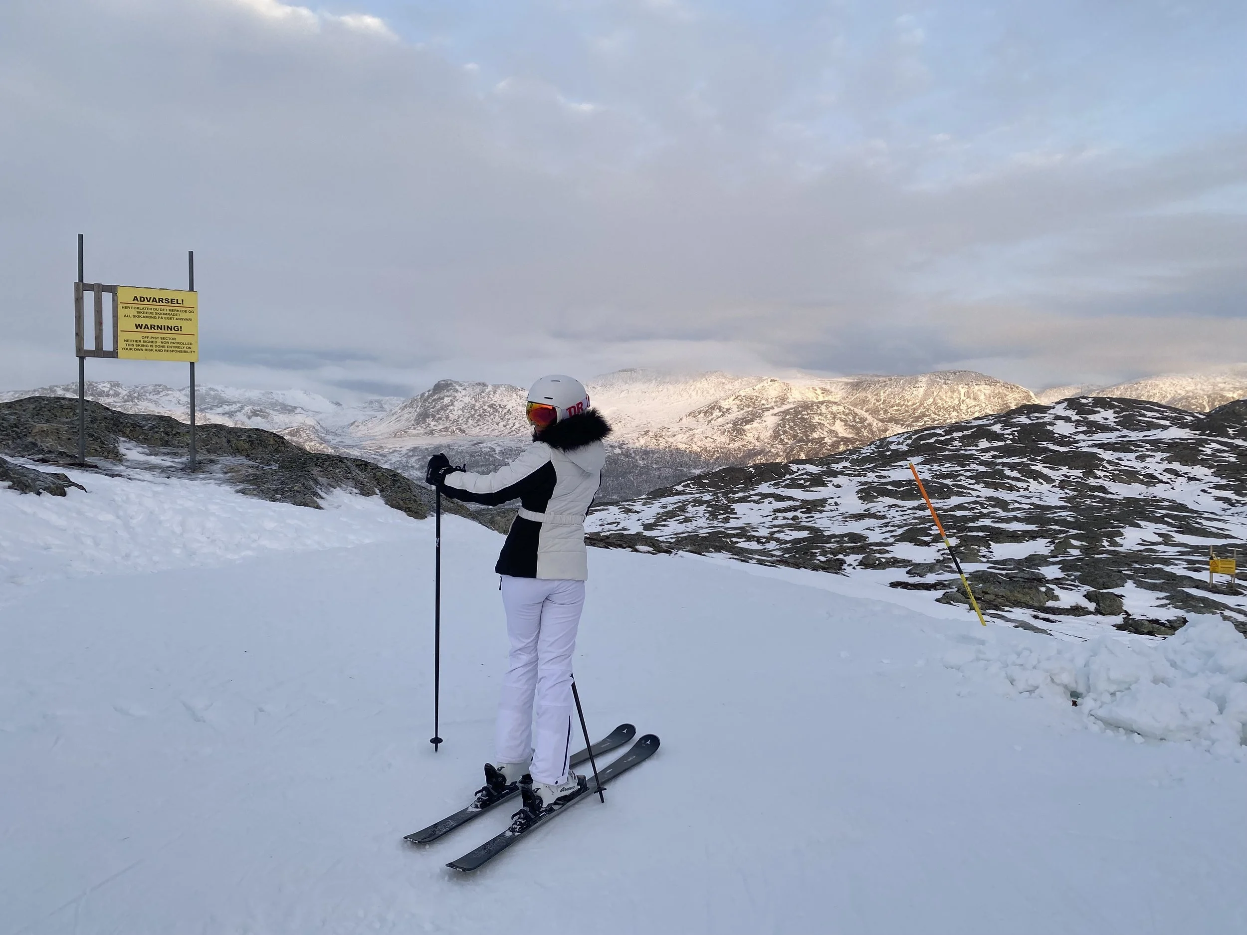 Skier in alpine terrain in Hemsedal in winter, standing on a high mountain slope with snow-covered peaks in the distance.