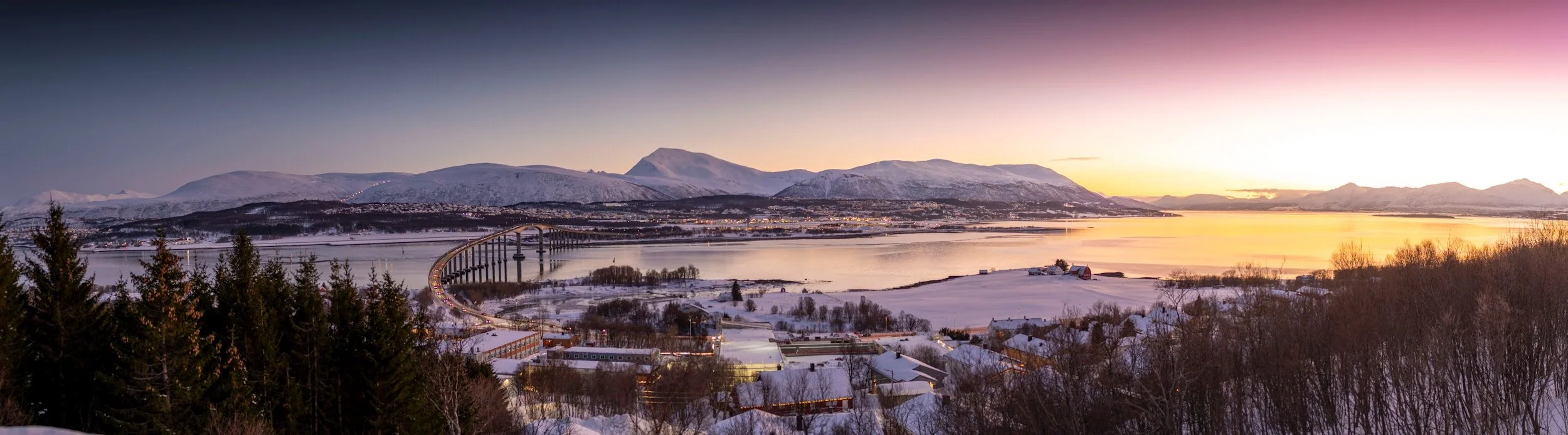 Winter view of Tromsø in Northern Norway, showing the city, fjords and surrounding mountains under Arctic winter light.